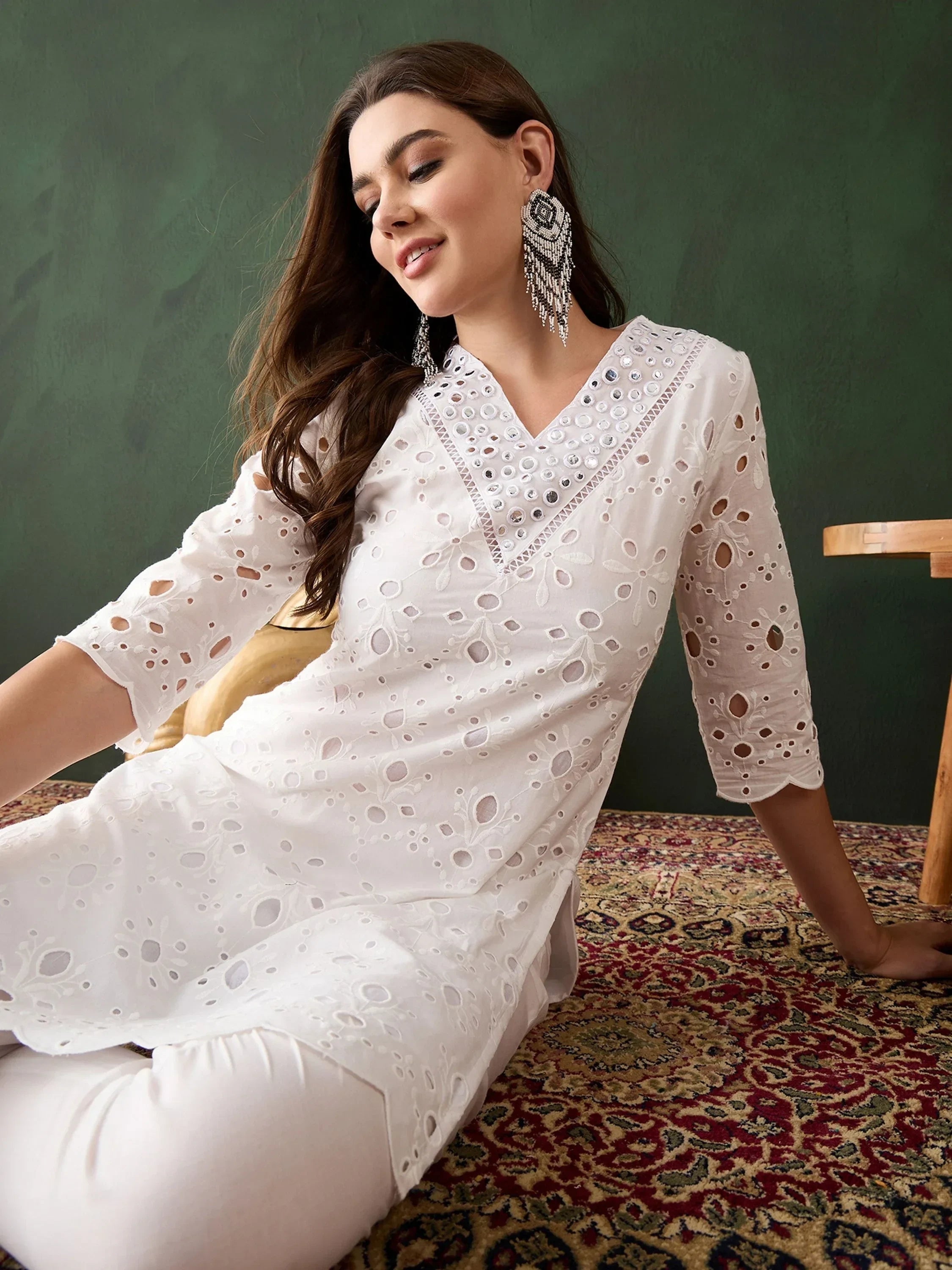 Woman in white embroidered kurta with mirror work, sitting on patterned carpet