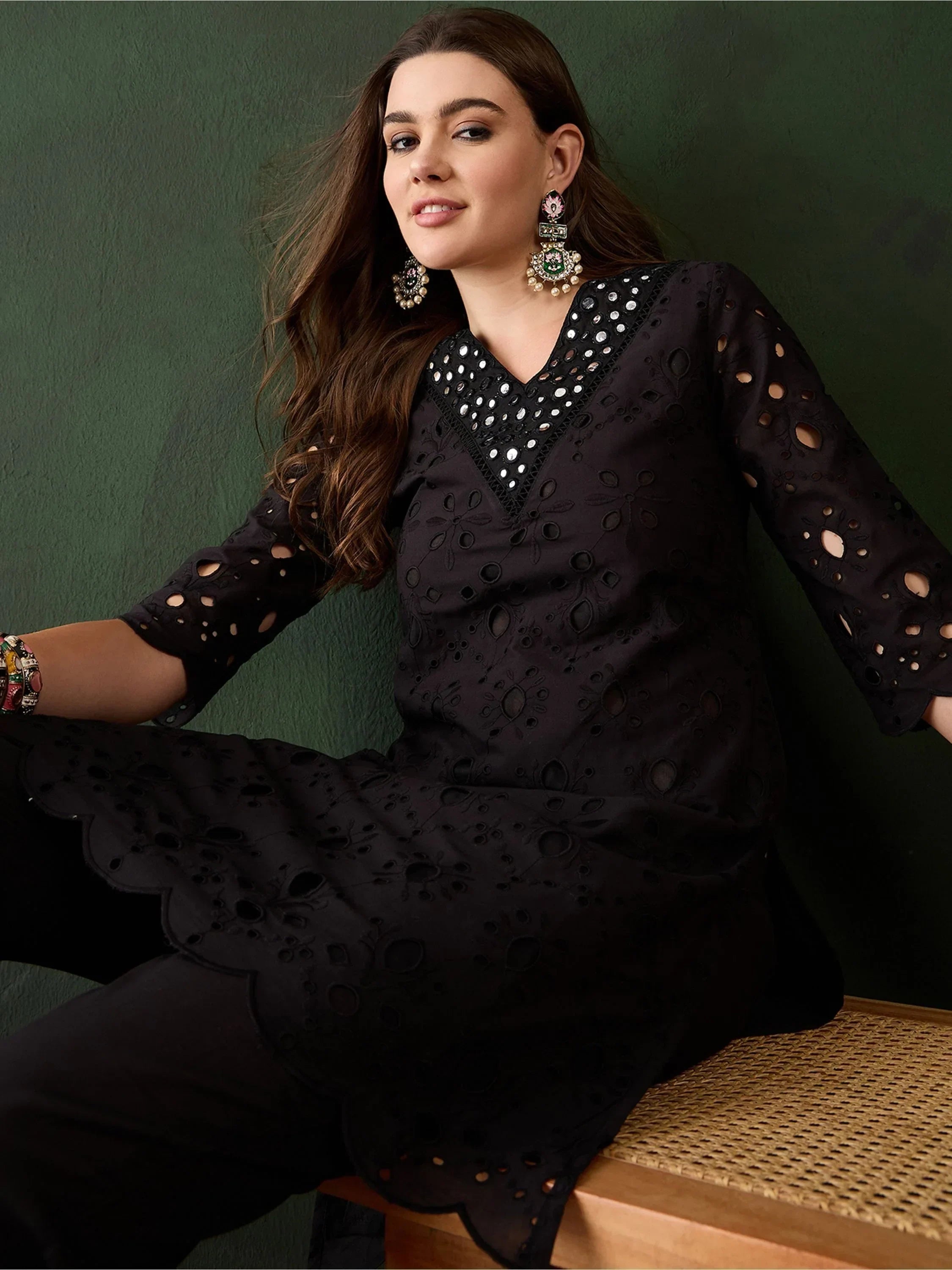 Woman wearing black embroidered kurti with mirror work, ethnic earrings, seated indoors
