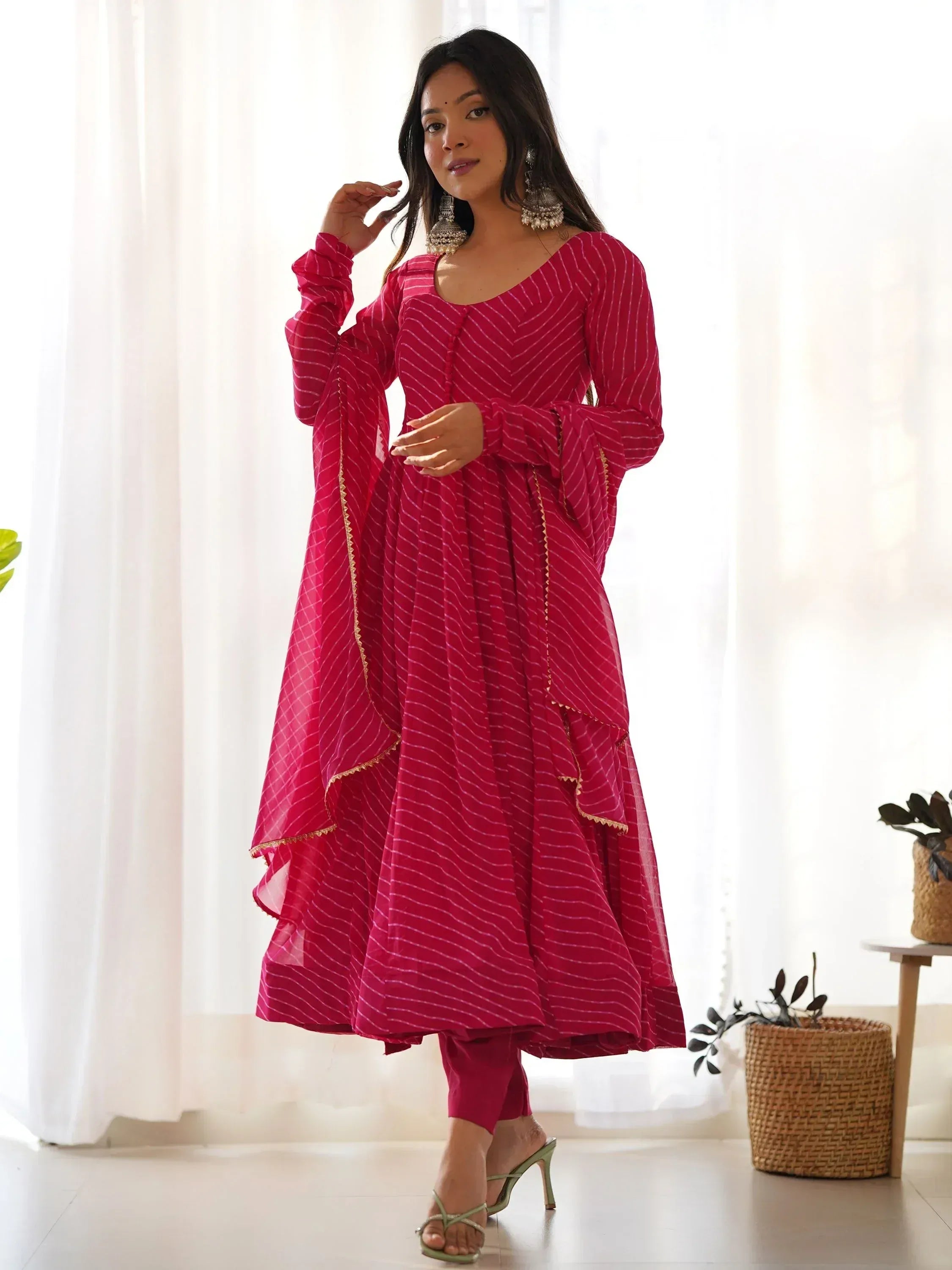 Pink striped ethnic gown with flared sleeves and gold trim, paired with matching pants and statement earrings.