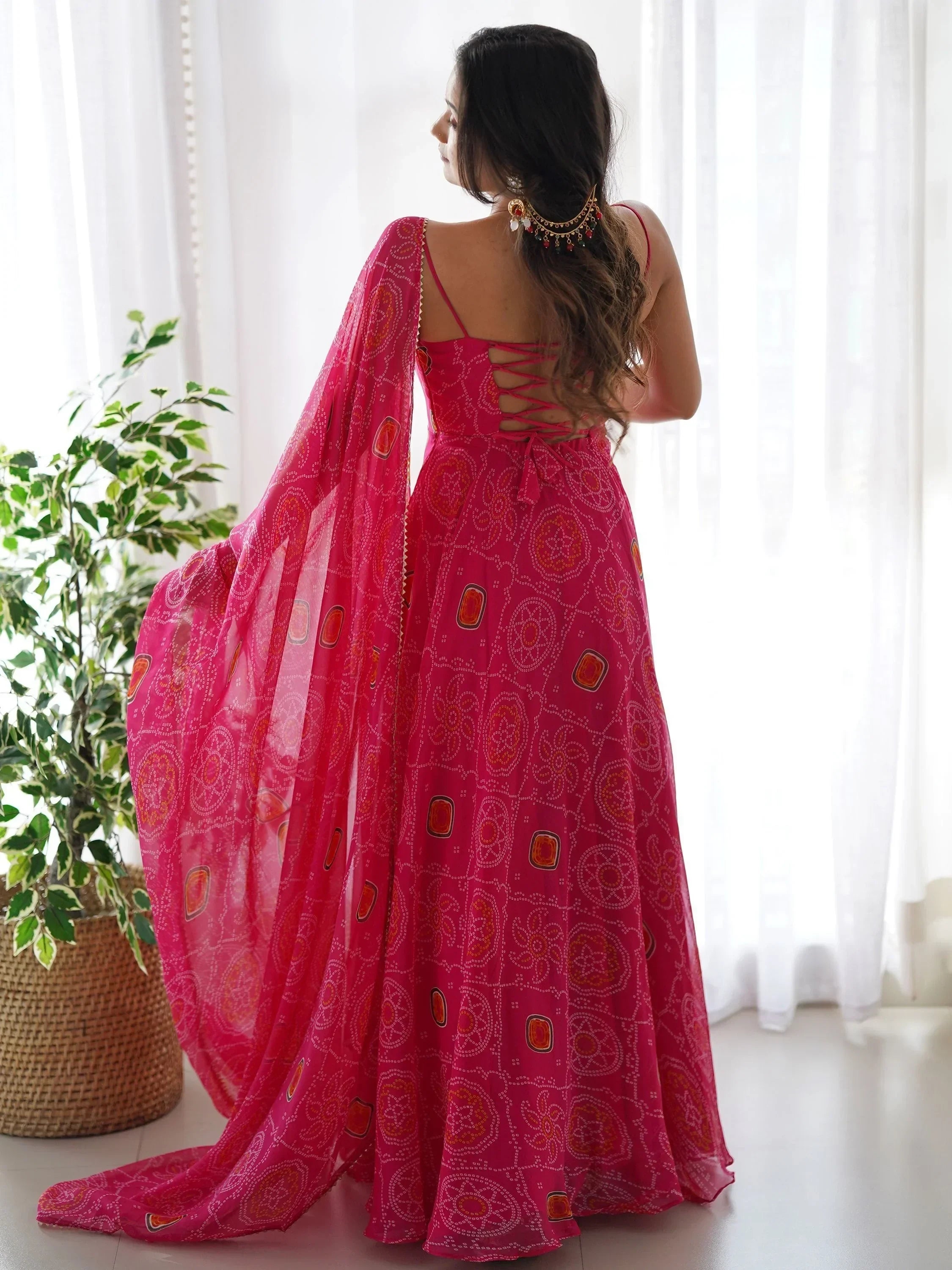 Woman in a vibrant pink traditional bandhani lehenga with back tie detailing, dupatta draped, standing indoors