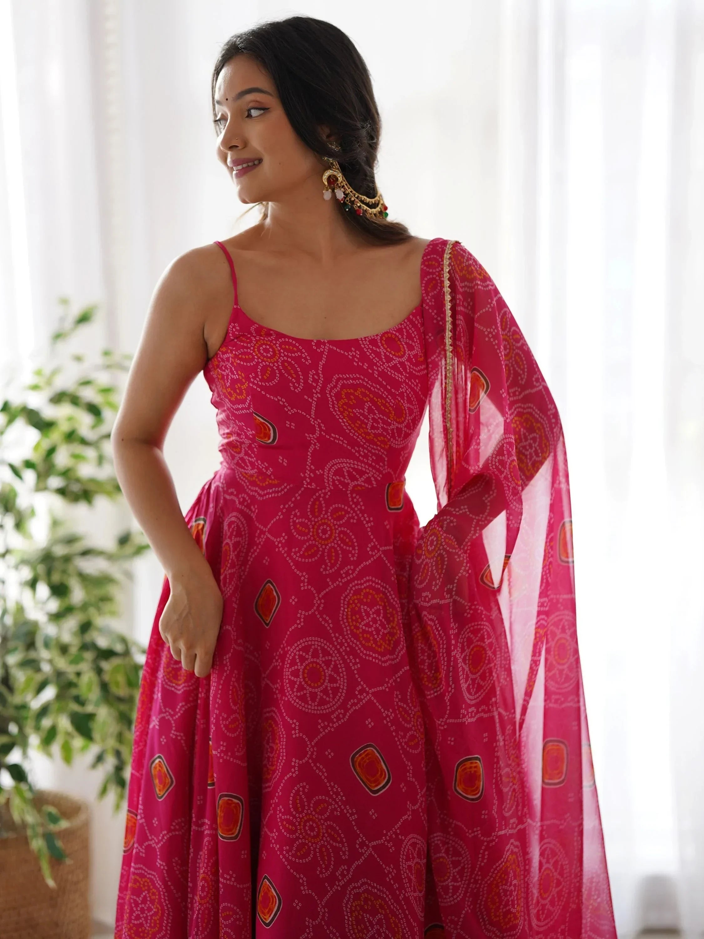 Woman in pink bandhani print ethnic gown with dupatta, traditional earrings, indoor setting