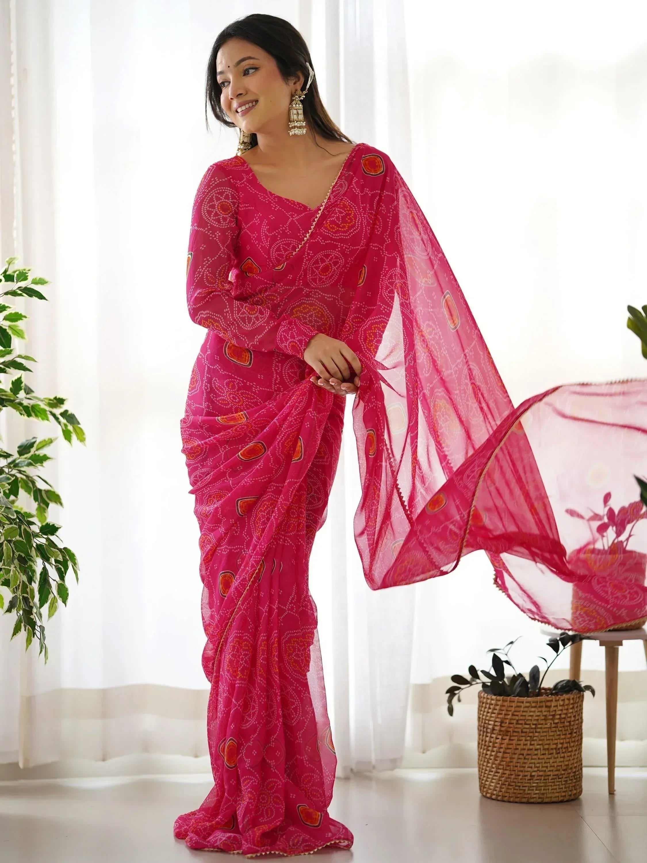 Woman in vibrant pink printed saree with gold trim, styled with ethnic jewelry, perfect for Indian ethnic wear occasions.