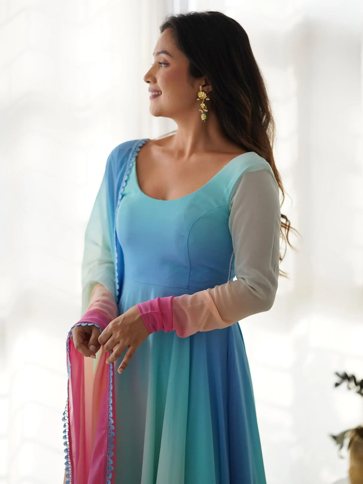 Woman in blue ombre ethnic gown with sheer sleeves and pink dupatta, styled with gold earrings