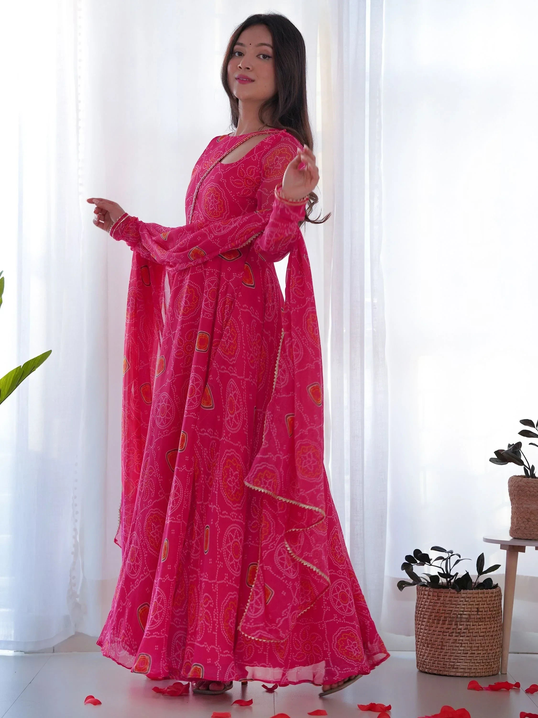 Woman in bright pink bandhani ethnic gown with dupatta, standing indoors on rose petals