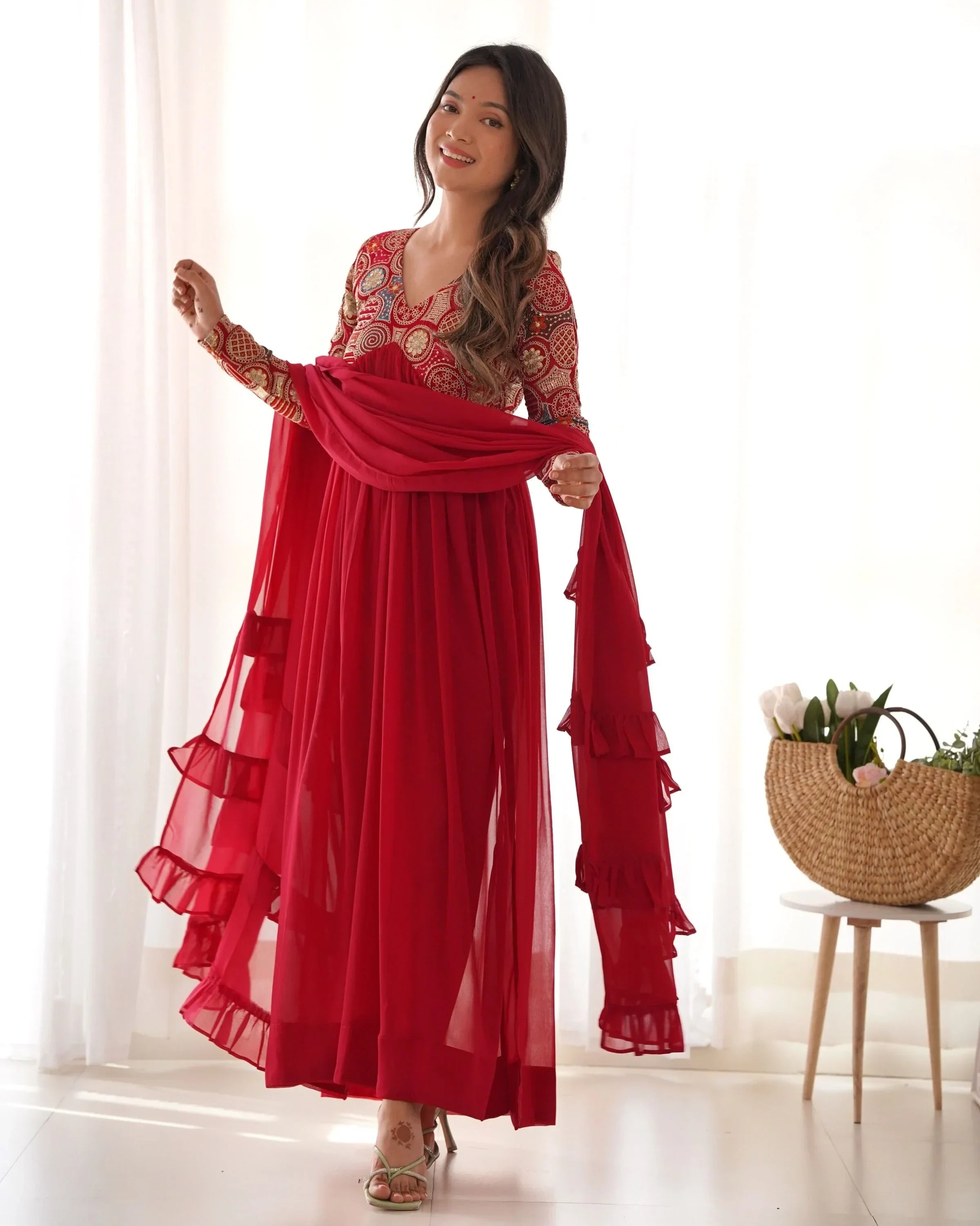 Woman in red embroidered Indian ethnic gown with dupatta, standing indoors