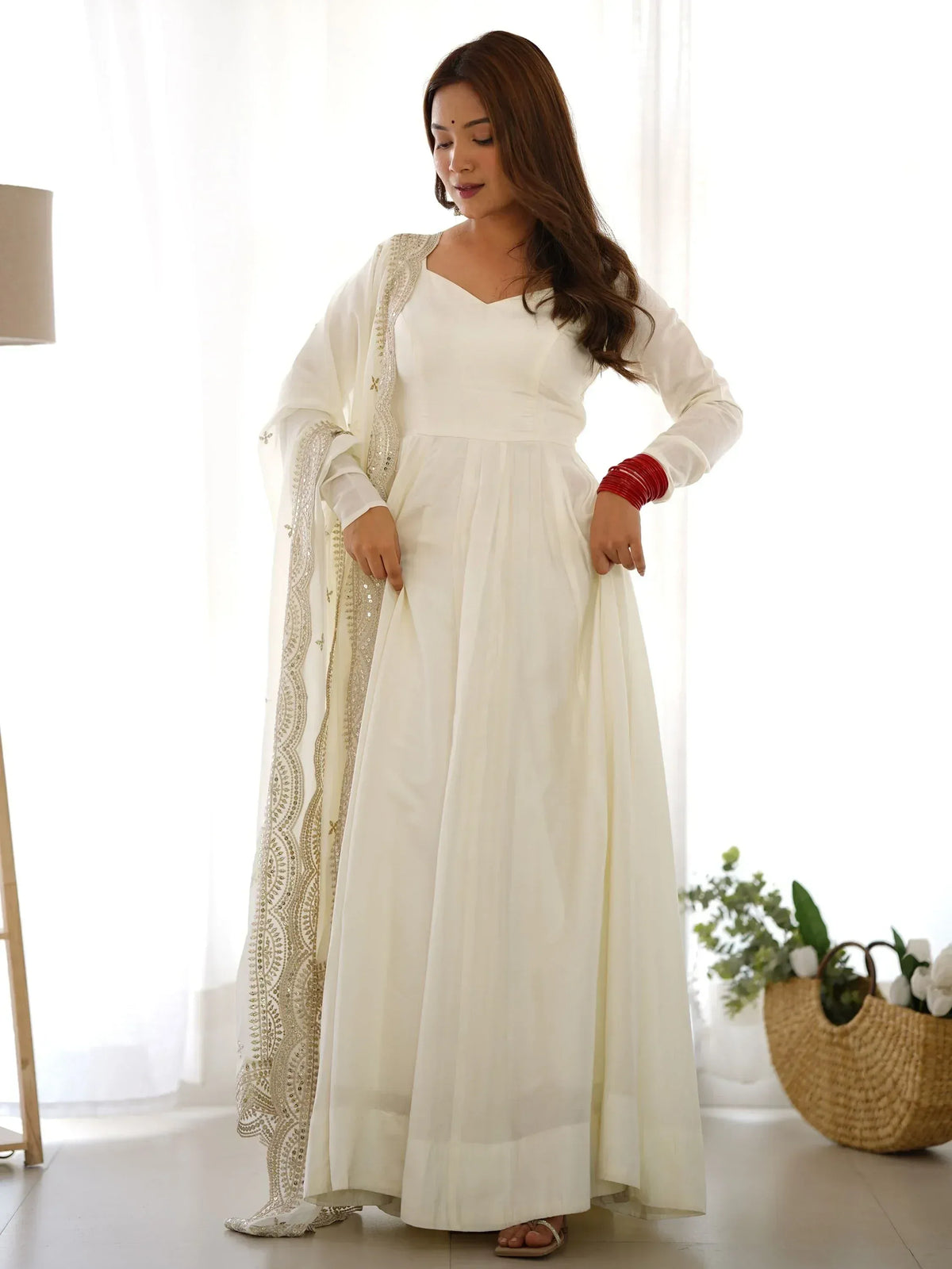 White ethnic gown with gold embroidery, paired with matching dupatta and red bangles for festive occasions