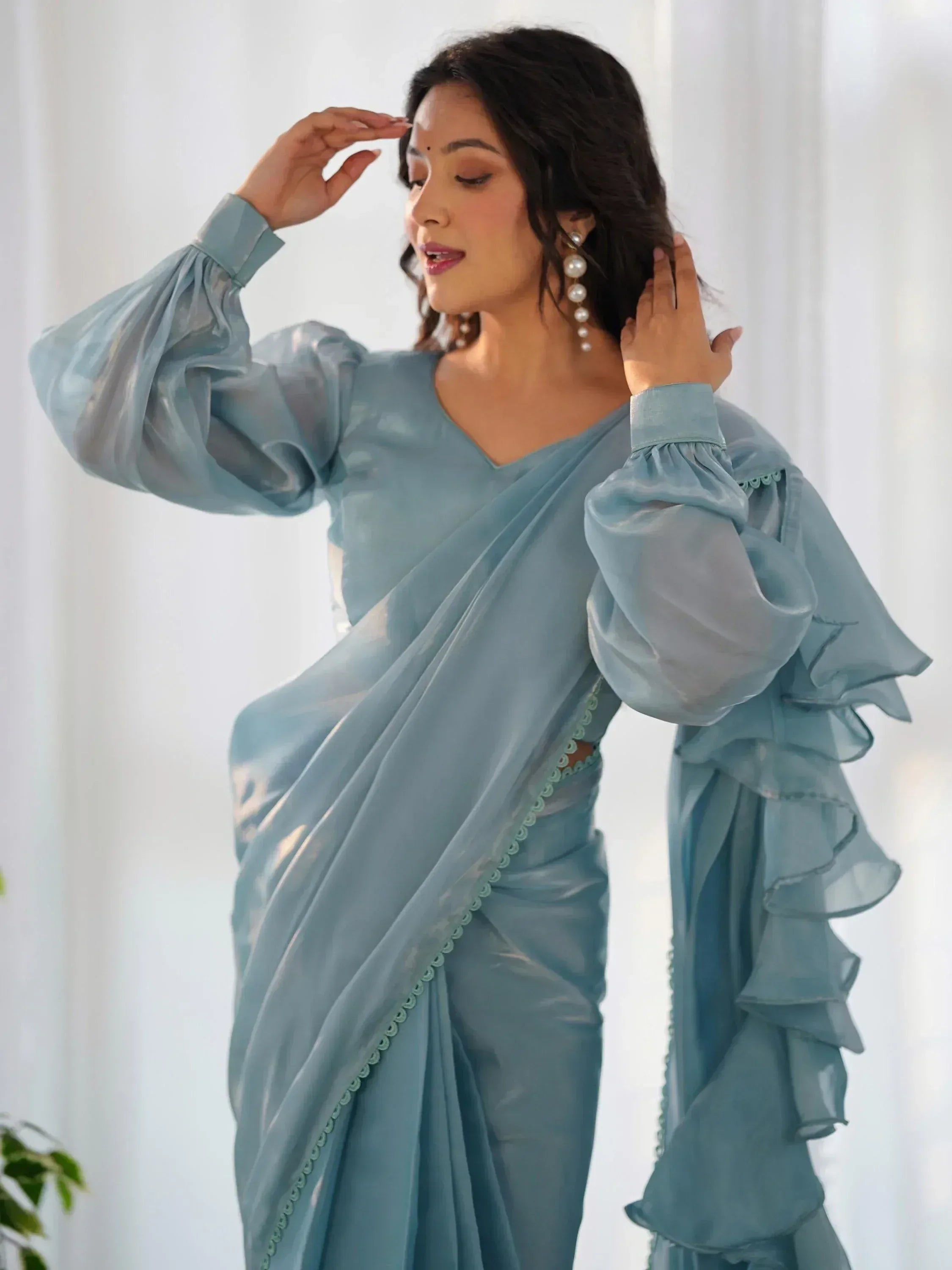 Woman in elegant light blue saree with ruffled sleeves and pearl earrings, showcasing Indian ethnic wear