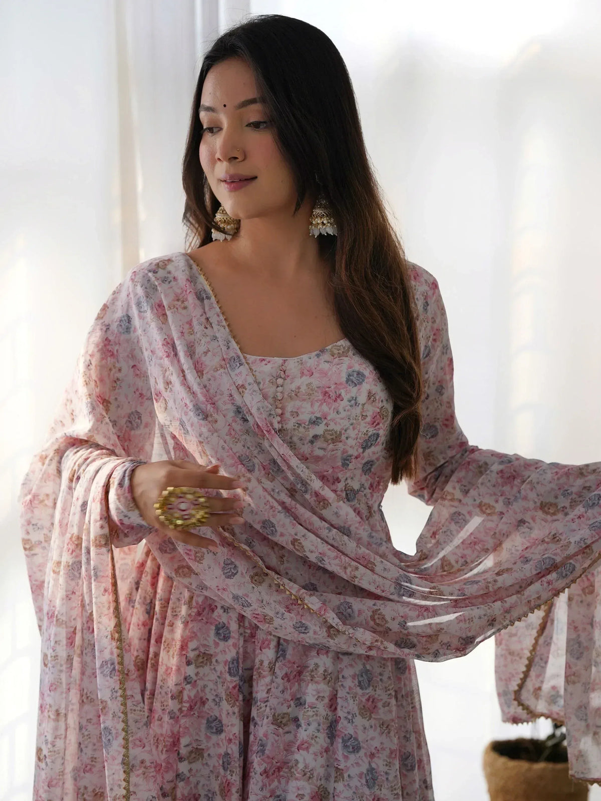 Woman in floral Indian ethnic gown with gold trim, styled with traditional earrings and ring