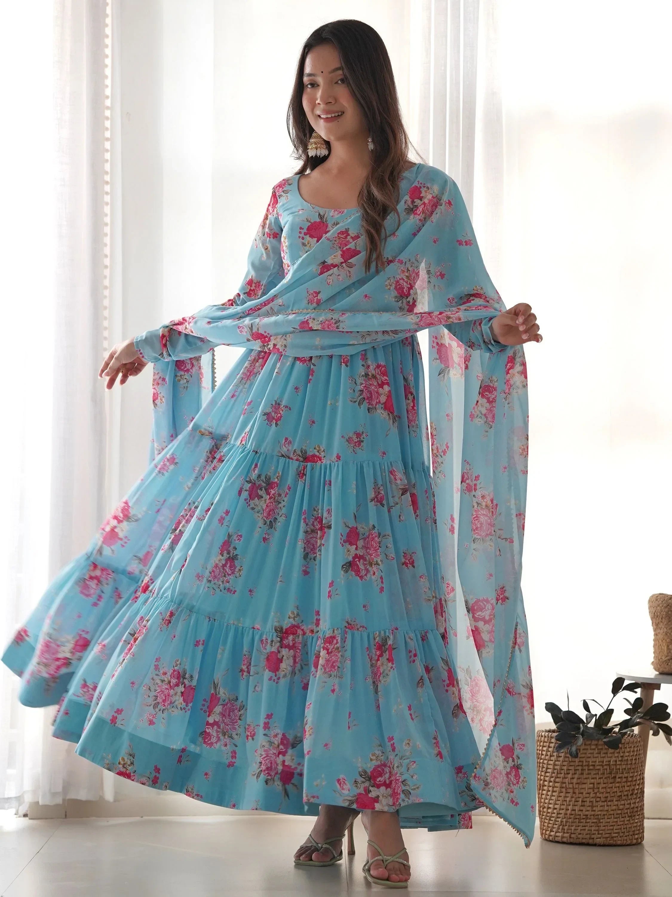 Woman in a light blue floral print ethnic gown with dupatta, posing indoors