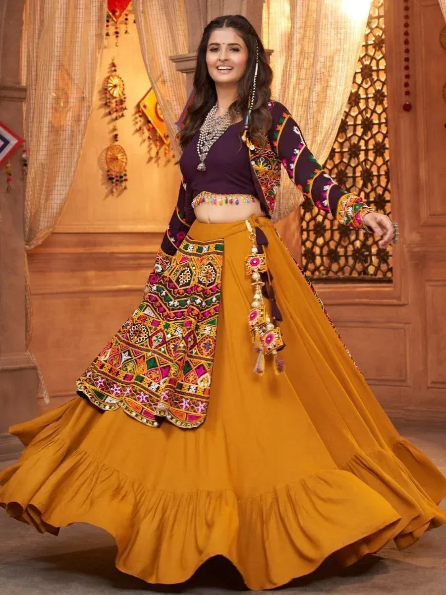 Woman in vibrant mustard yellow lehenga choli with colorful embroidery and mirror work, perfect for Indian ethnic occasions.