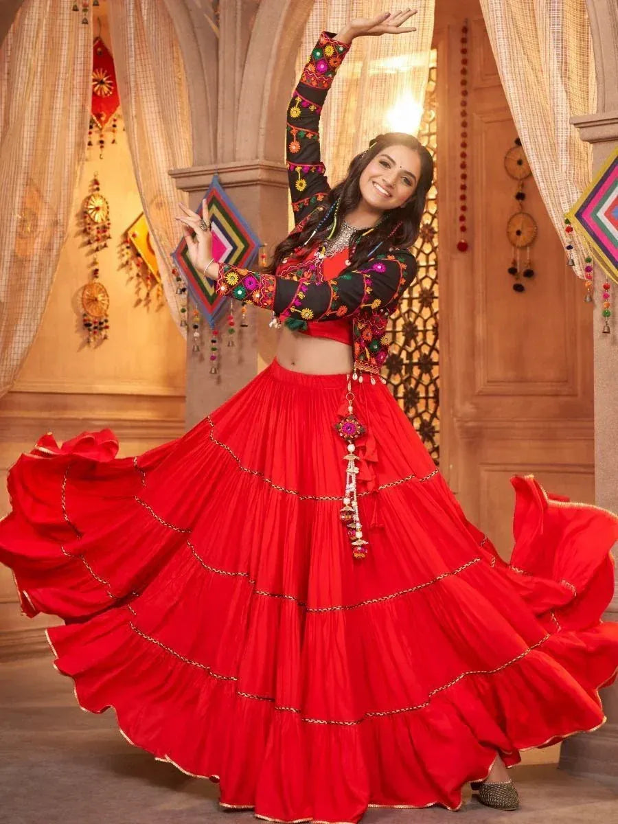 Woman dancing in vibrant red tiered lehenga with embroidered black blouse, perfect for Indian ethnic occasions.