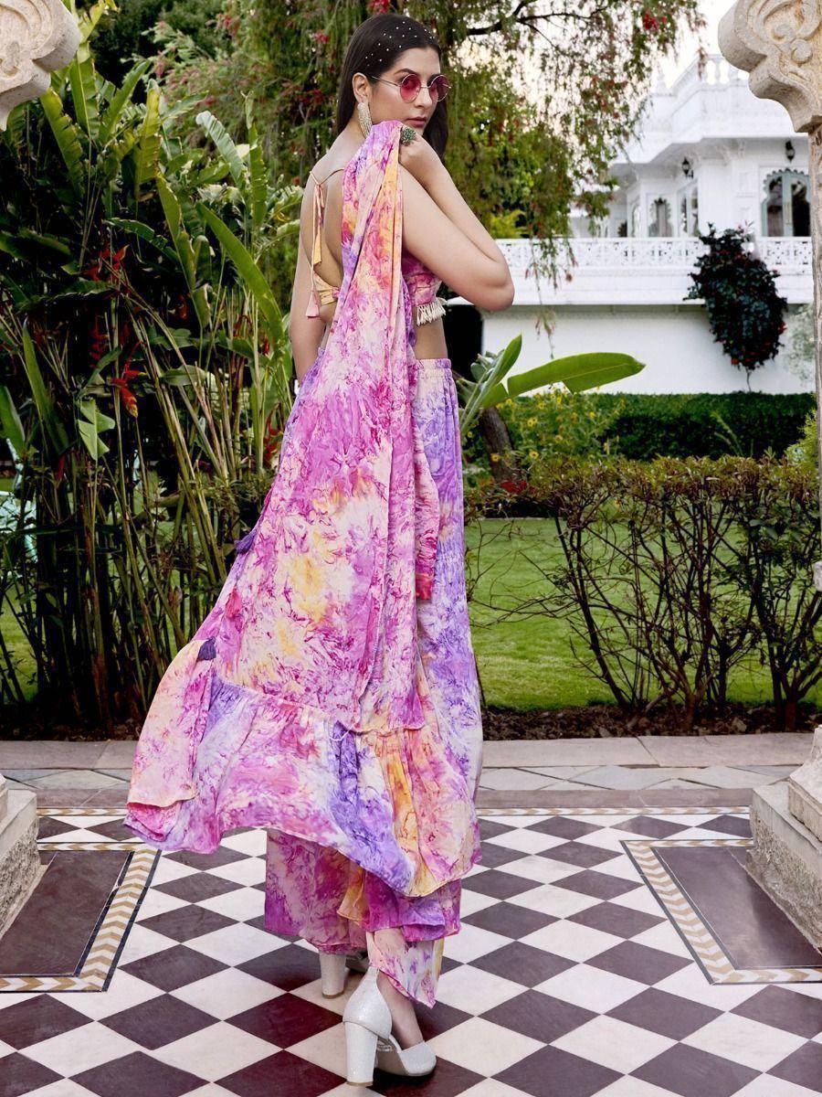 Woman in vibrant tie-dye ethnic gown with ruffled layers, styled for Indian occasions, garden backdrop