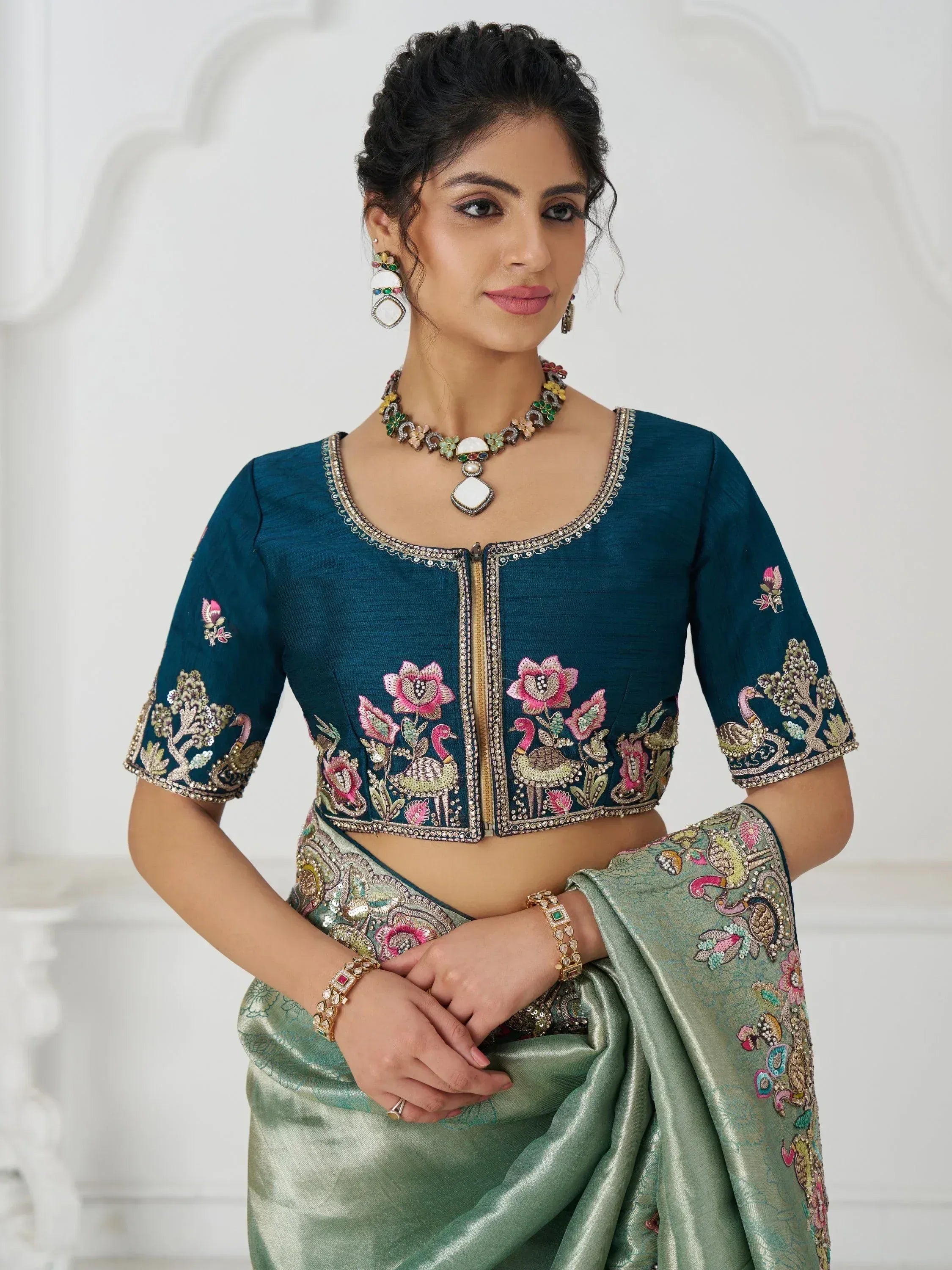 Teal embroidered blouse with floral and peacock motifs, paired with green saree, perfect for Indian ethnic wear.