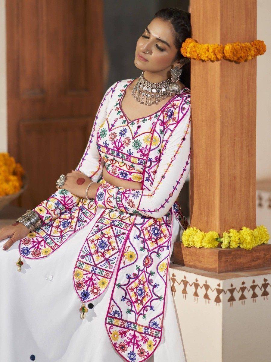 White embroidered ethnic kurta with colorful floral patterns, paired with traditional jewelry and marigold decor