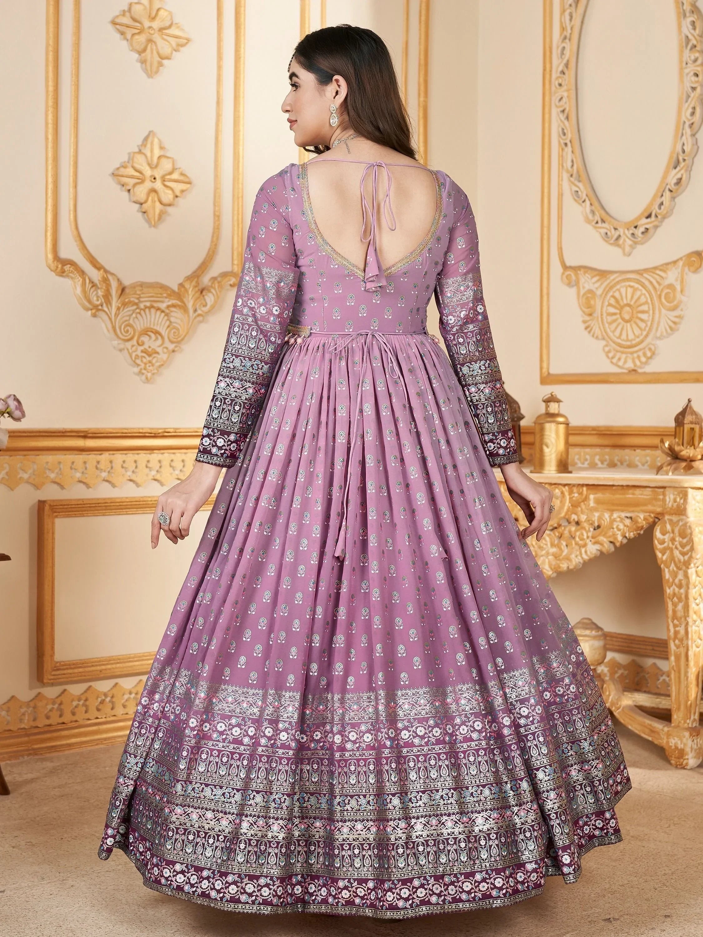 Woman in a mauve embroidered ethnic gown with open back and long sleeves, standing indoors