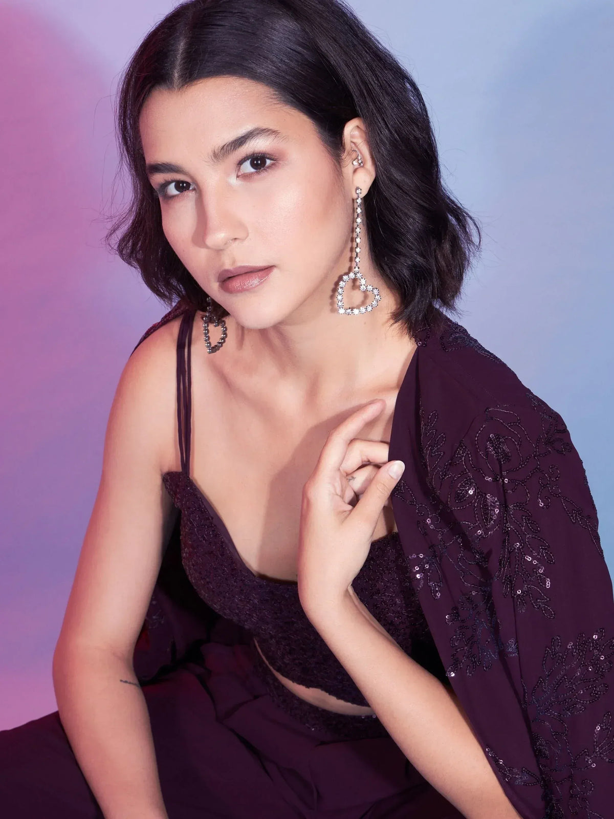 Elegant woman in purple sequined ethnic gown with heart-shaped earrings, perfect for Indian festive occasions.