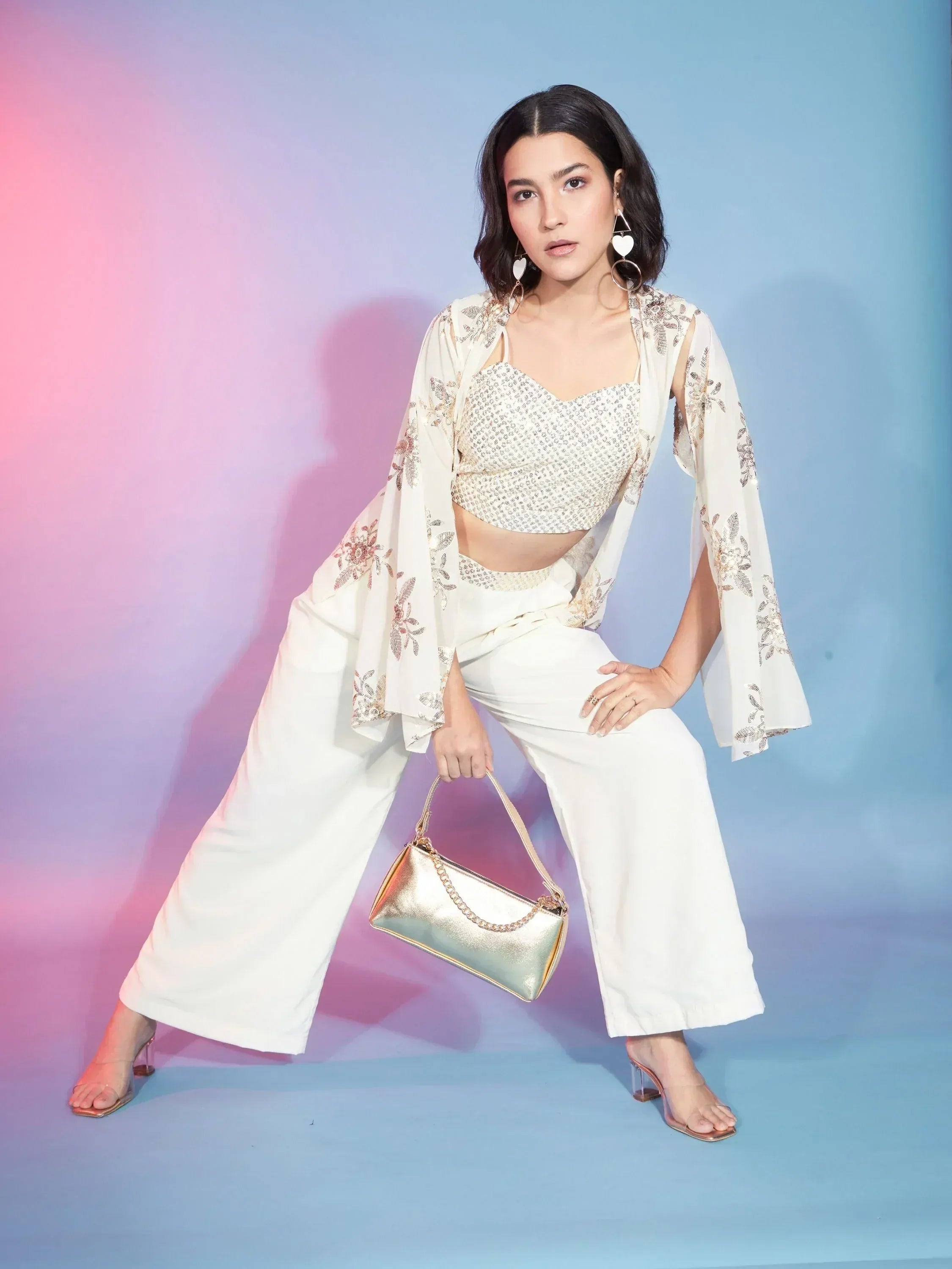 White ethnic crop top with floral jacket, wide pants, and gold handbag for festive occasions
