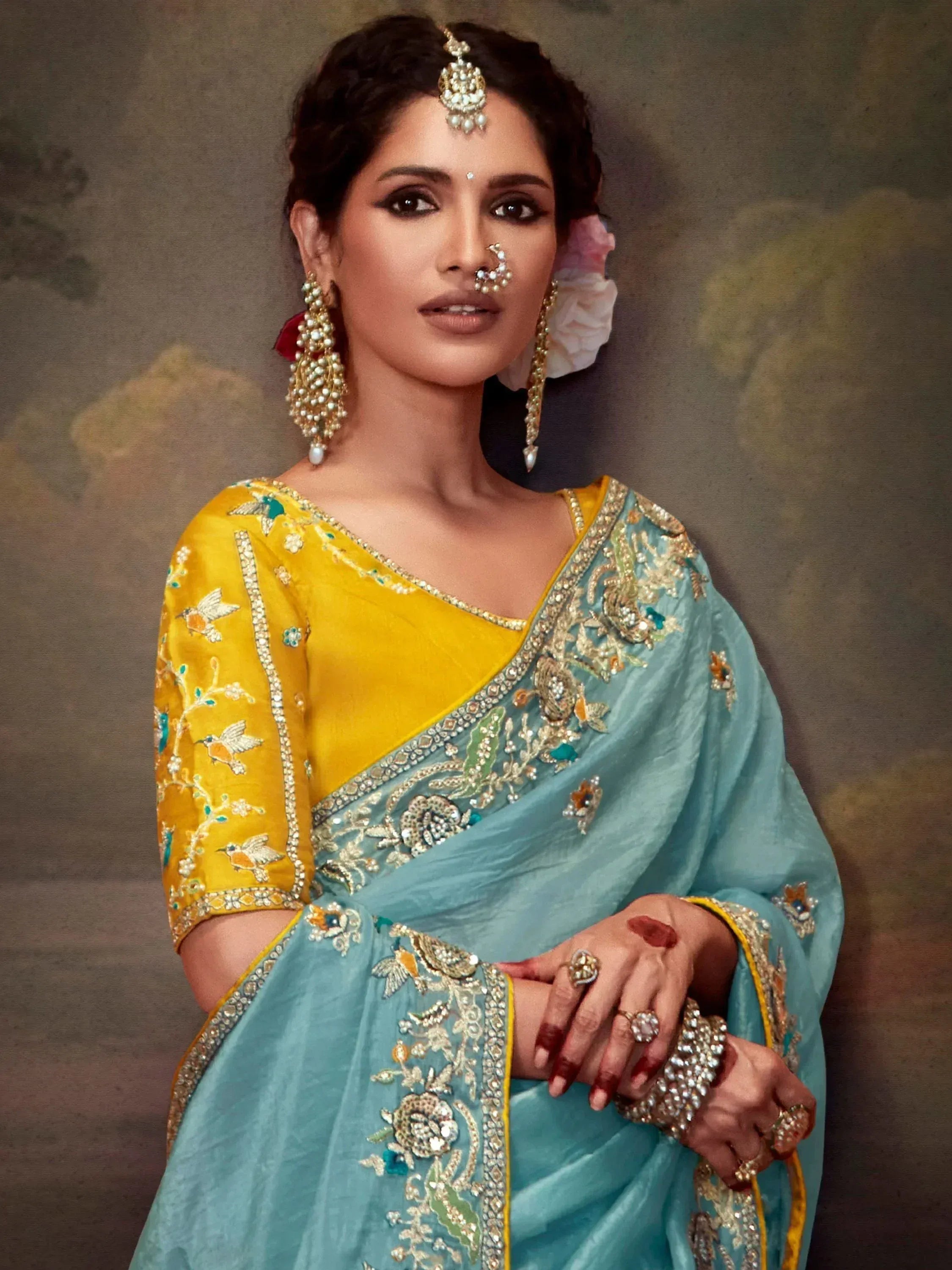 Elegant Indian woman in turquoise and yellow embroidered saree with traditional jewelry and floral hair accessory