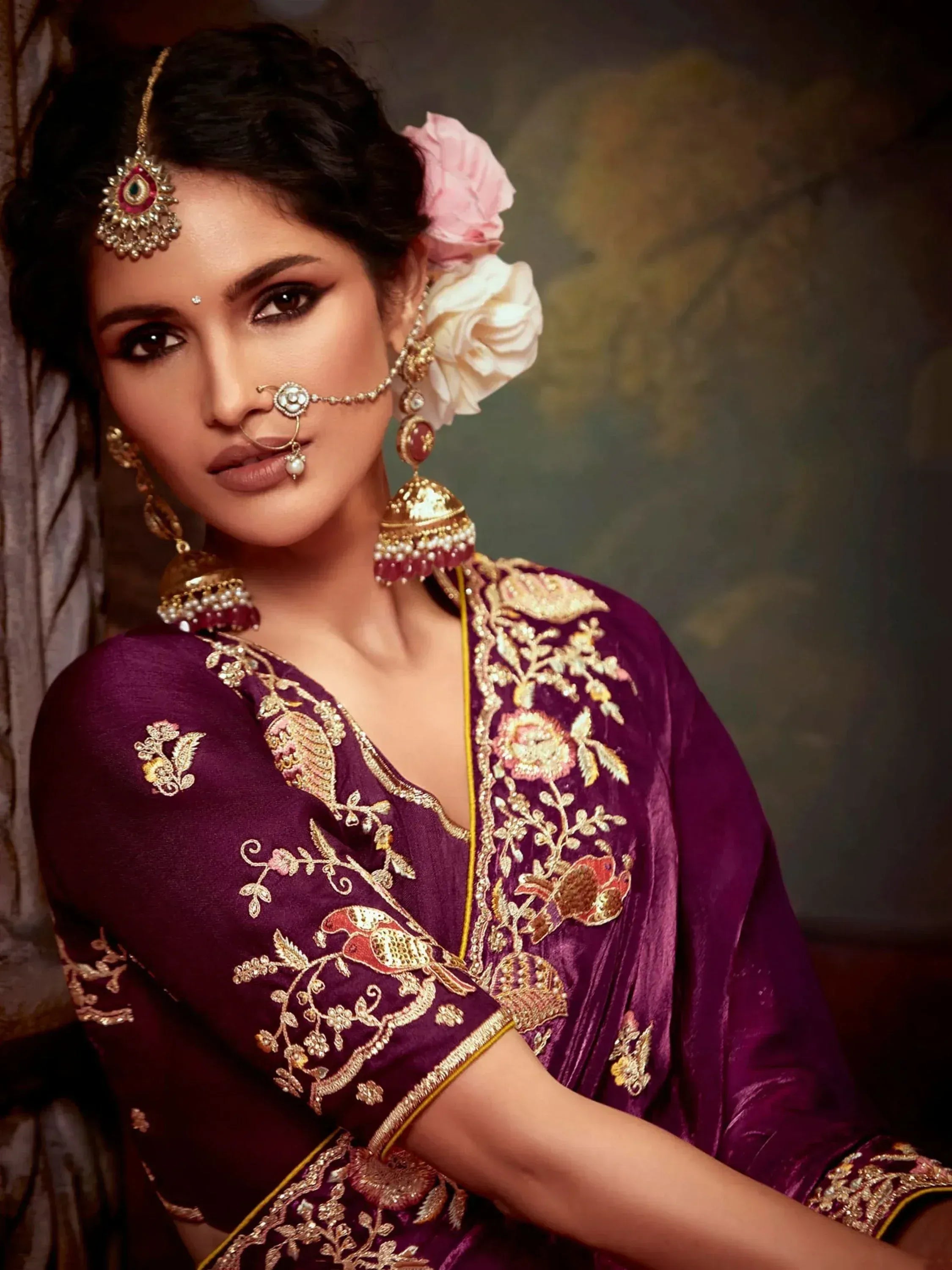 Woman in purple embroidered Indian ethnic gown with gold jewelry and floral hair accessory