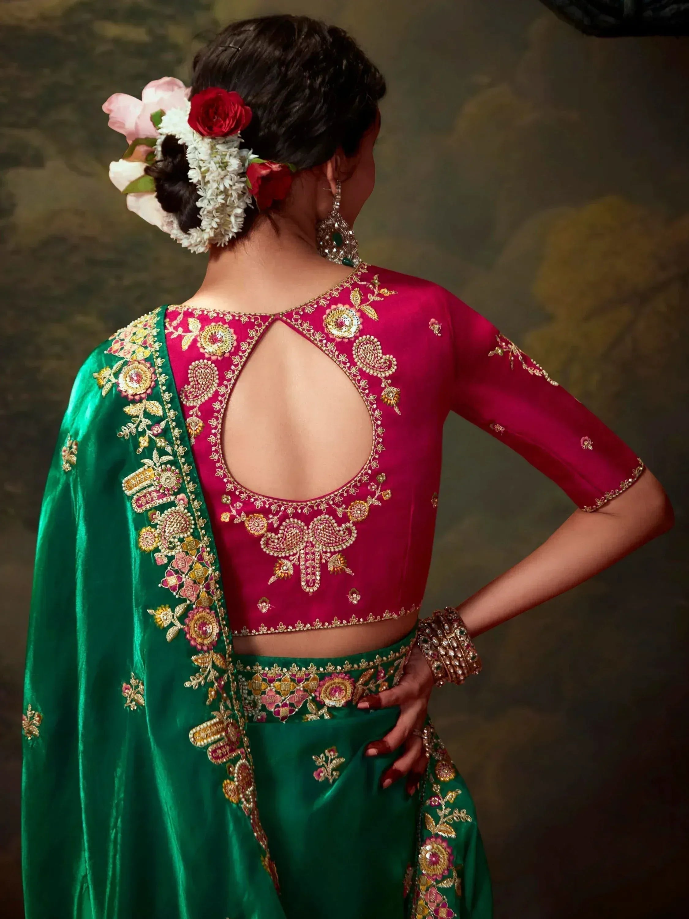 Back view of woman in green and pink embroidered lehenga choli with floral hair accessories