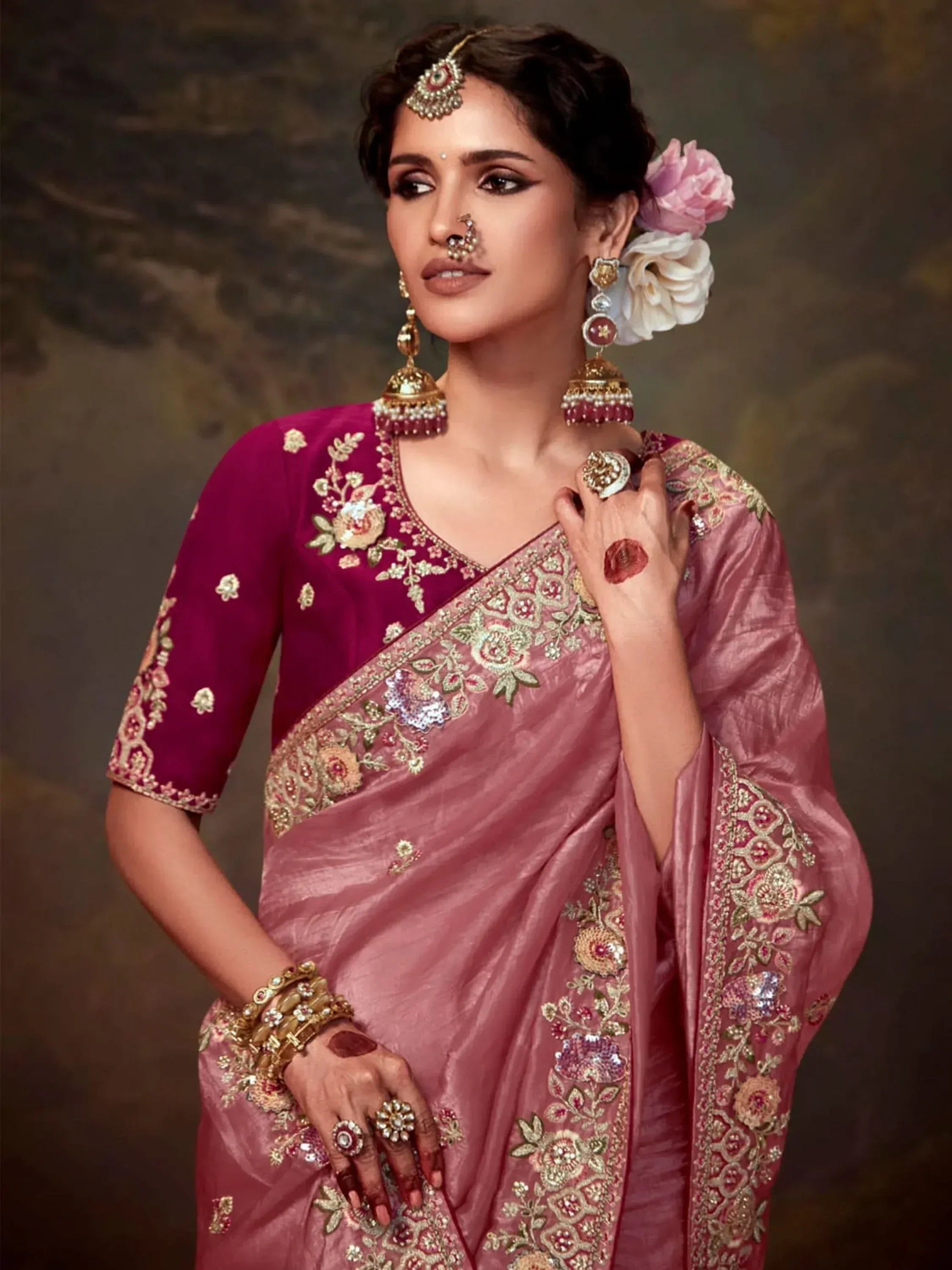 Elegant woman in embroidered pink saree with gold jewelry and floral hair accessories, showcasing Indian ethnic wear.