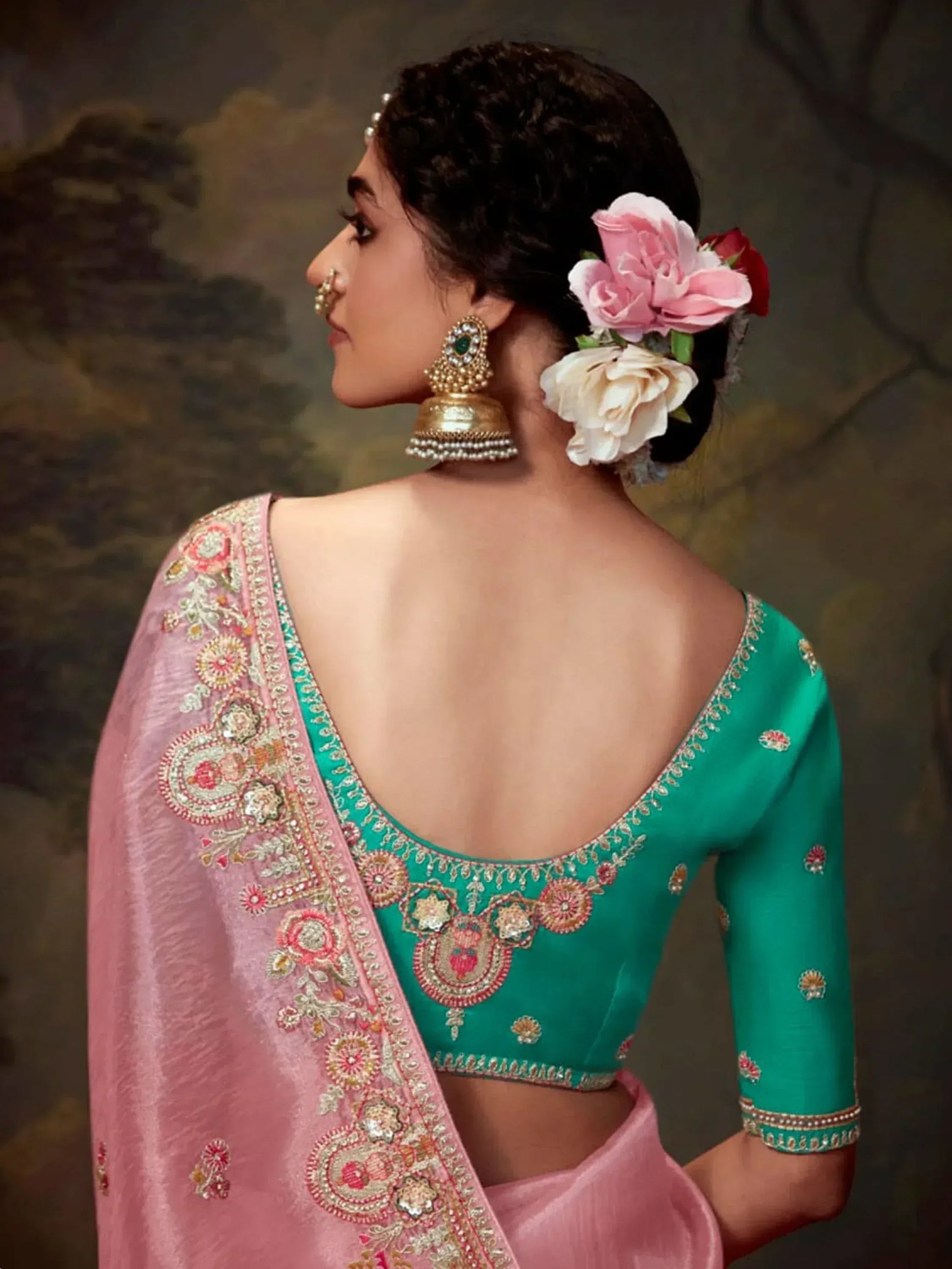 Green embroidered blouse with pink saree, floral hair accessory, and gold jhumka earrings for Indian ethnic wear