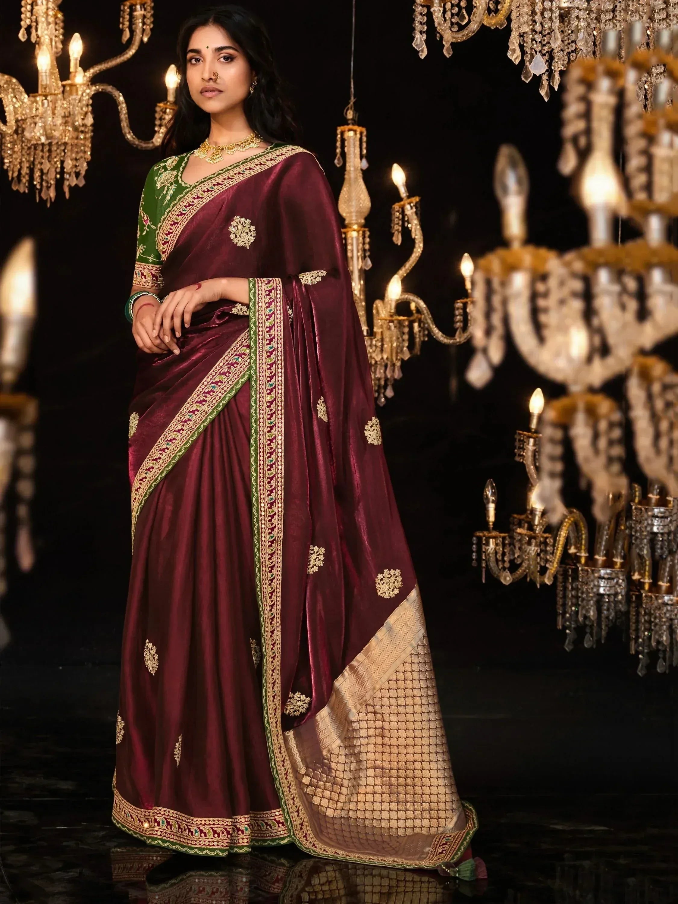 Maroon velvet saree with green blouse, gold embroidery, and chandelier backdrop