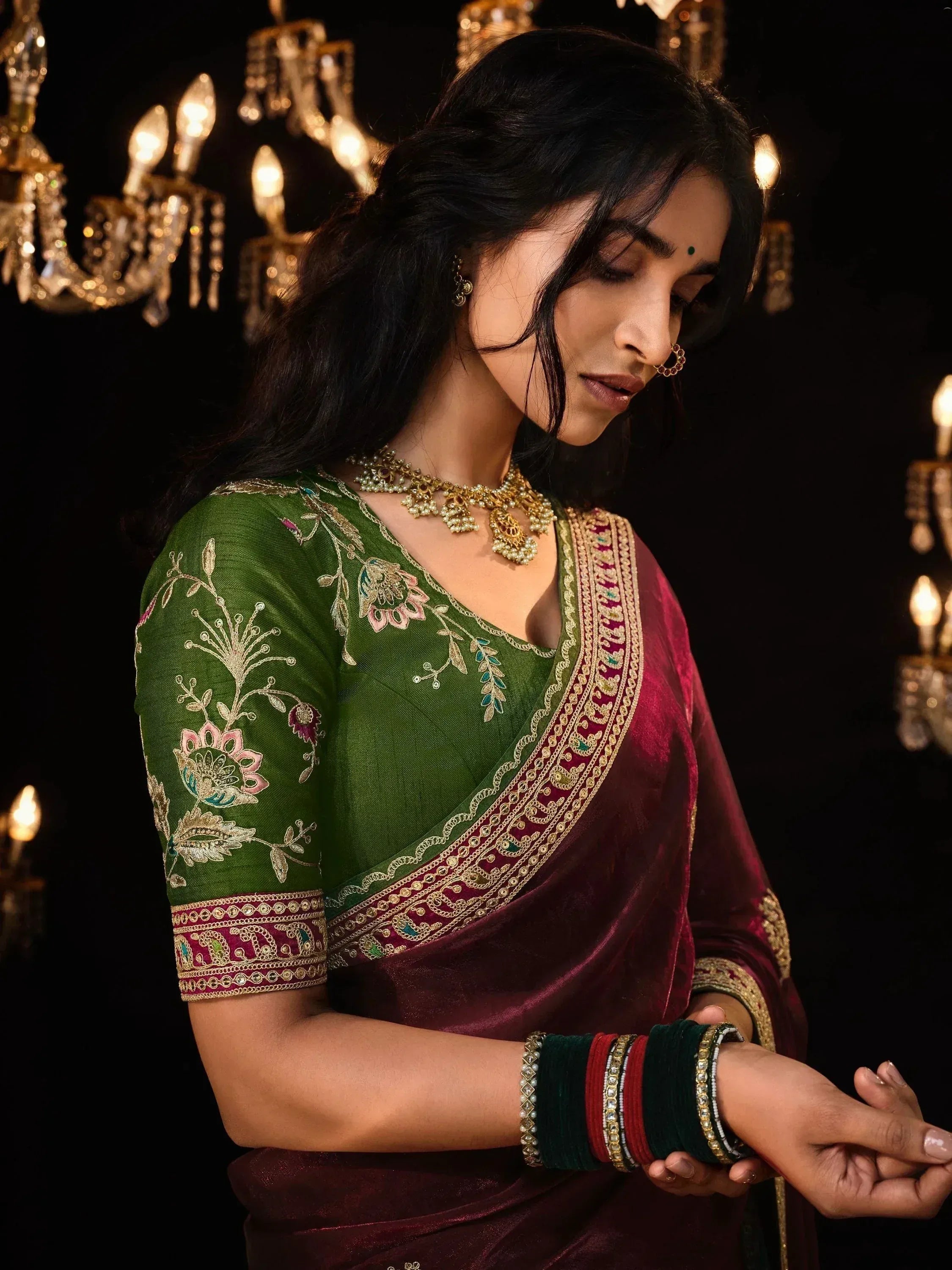 Elegant woman in green and maroon embroidered saree with gold jewelry, perfect for Indian ethnic occasions.