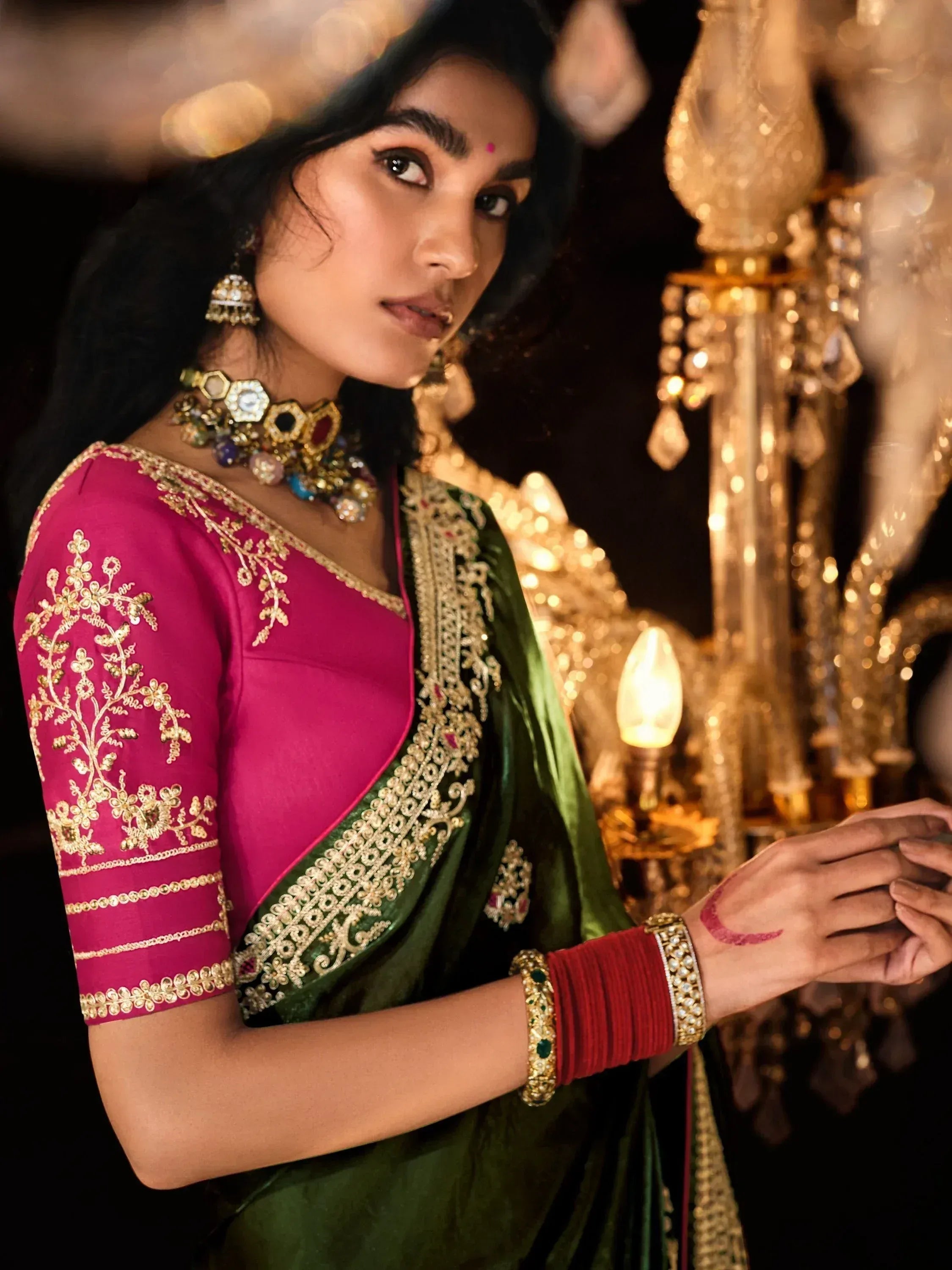 Woman in pink and green embroidered saree with gold jewelry, festive Indian ethnic wear