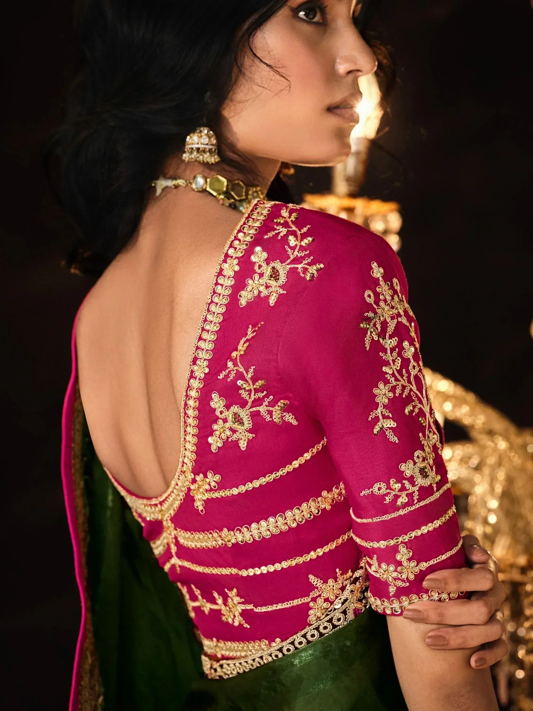 Pink embroidered saree blouse with gold floral work, backless design, paired with green saree and traditional jewelry