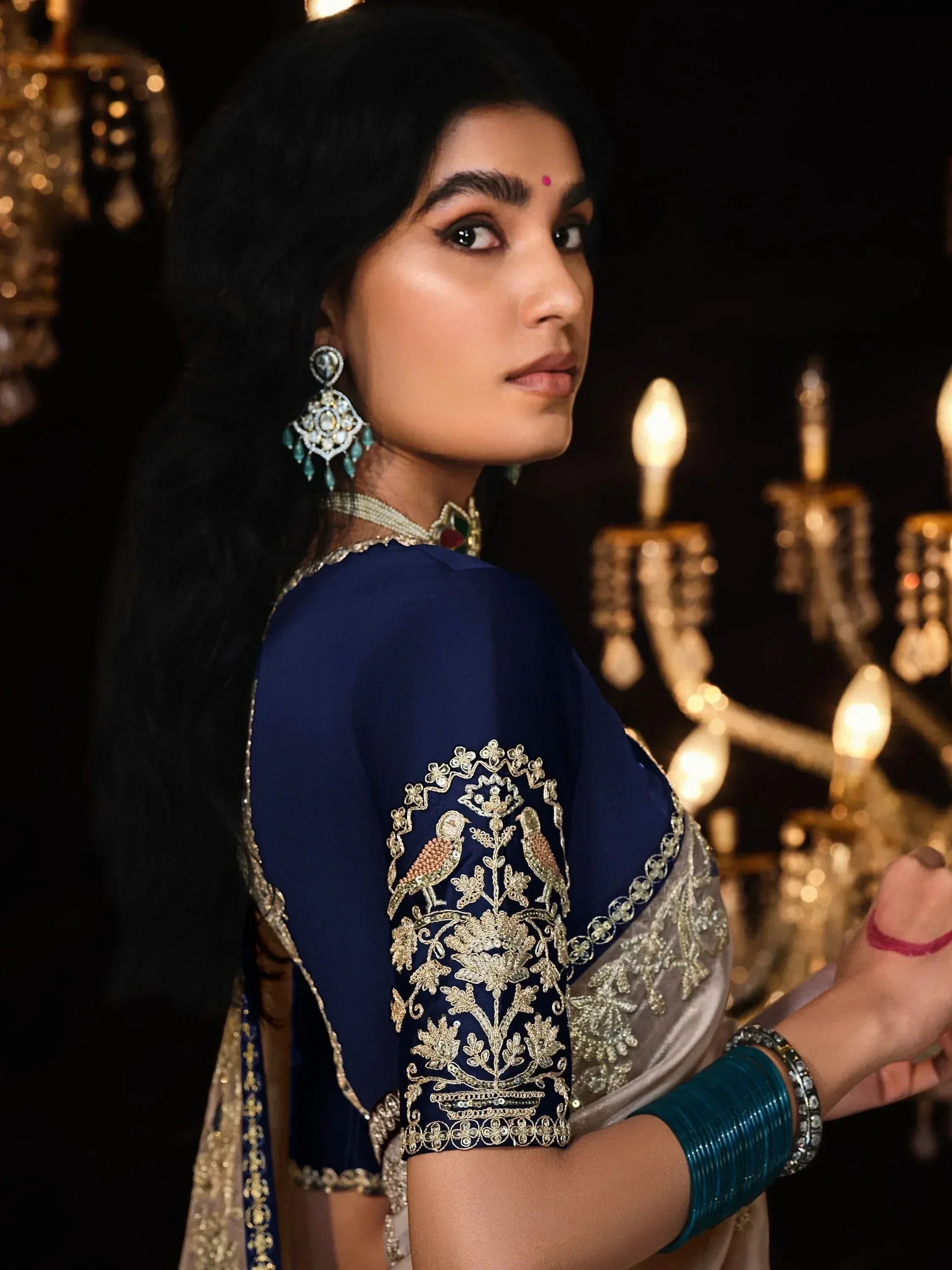 Woman in navy blue embroidered saree with gold bird motifs, traditional Indian ethnic wear, statement earrings, and bangles.