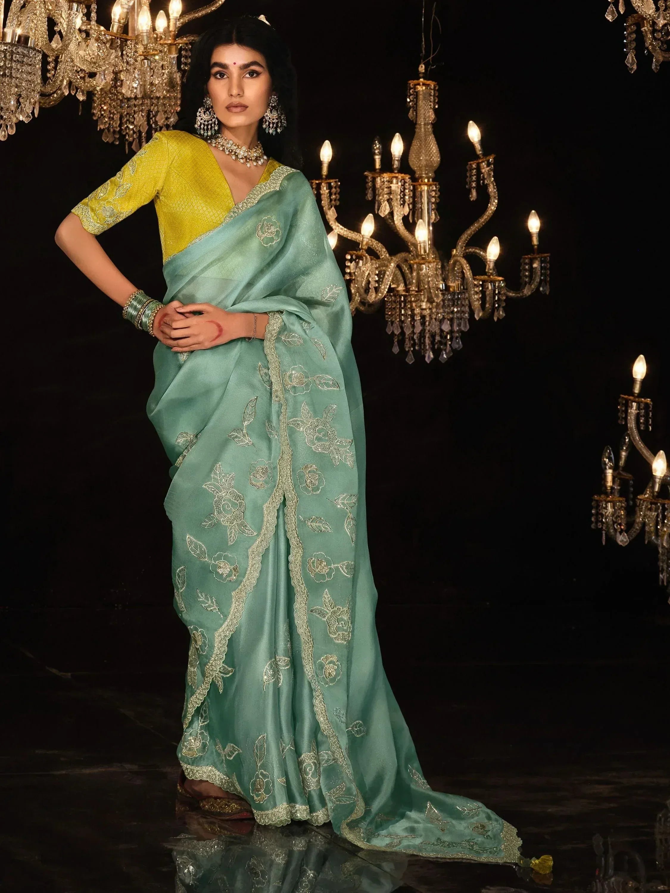 Elegant mint green saree with gold floral embroidery and yellow blouse, styled with chandelier backdrop for festive occasions.