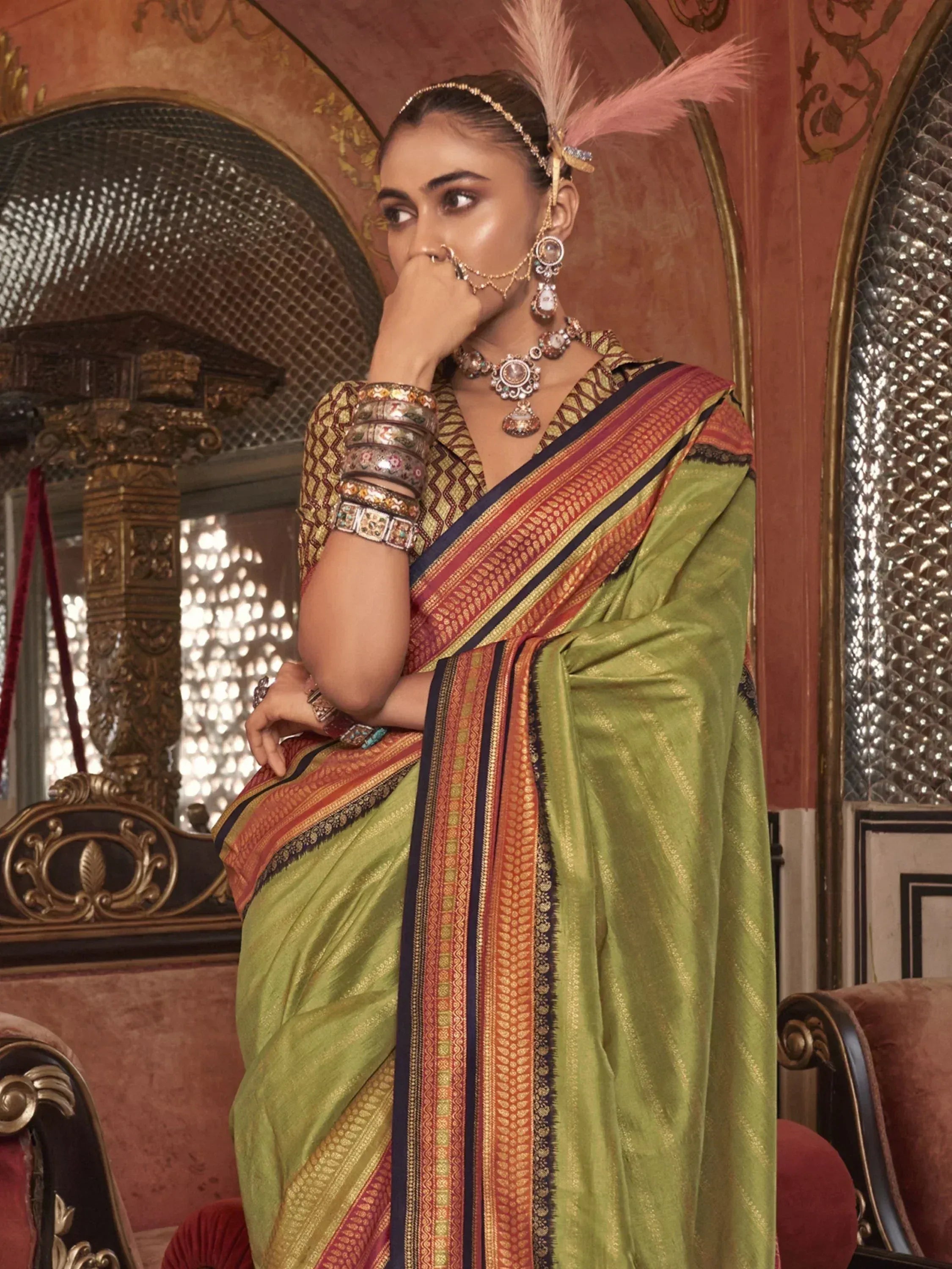 Elegant green saree with intricate border, paired with traditional jewelry and feather headpiece