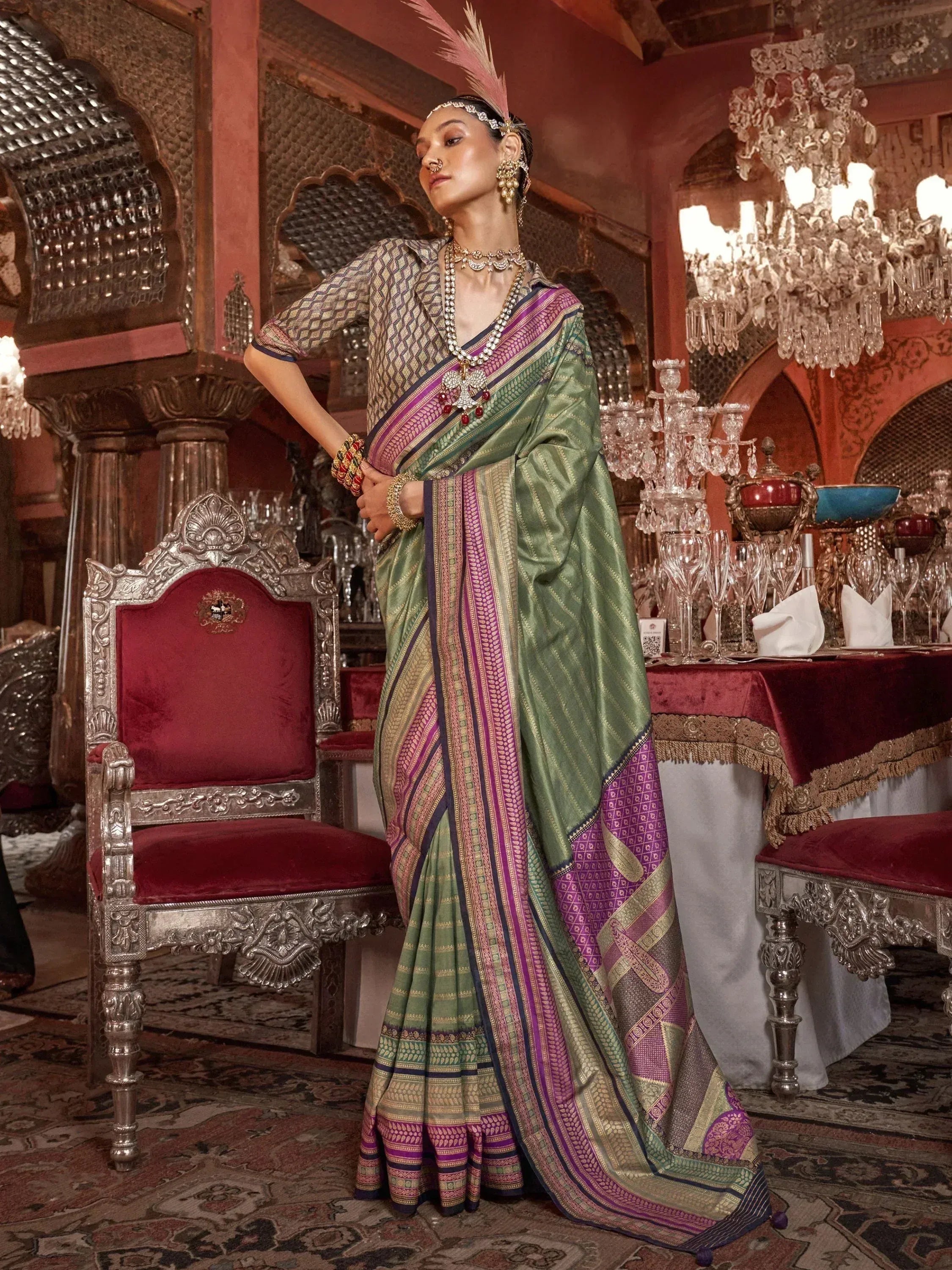 Elegant green and purple saree with intricate patterns, paired with traditional jewelry and a feathered headpiece.