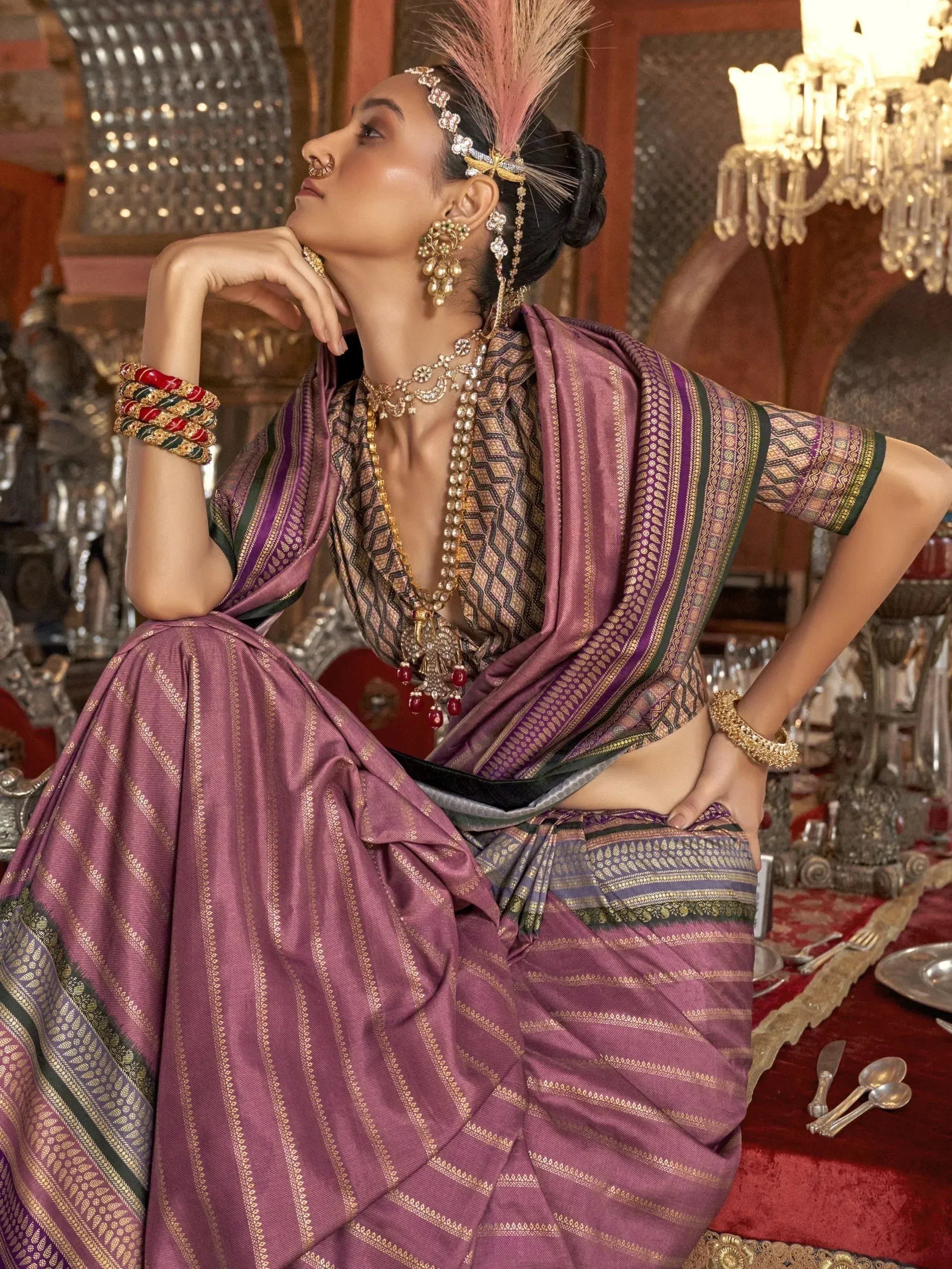 Elegant woman in purple ethnic saree with gold embroidery, traditional jewelry, and feather headpiece, styled for festive occasions.