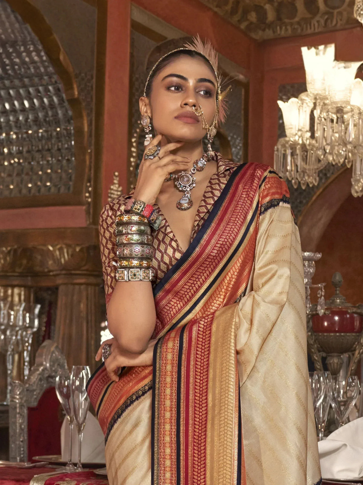 Elegant woman in traditional Indian saree with intricate gold and red borders, adorned with vintage jewelry in a luxurious setting