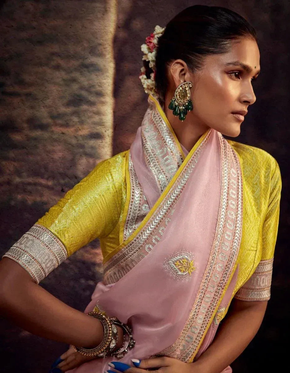 Woman in yellow blouse and pink saree with silver border, floral hair accessory, and traditional jewelry