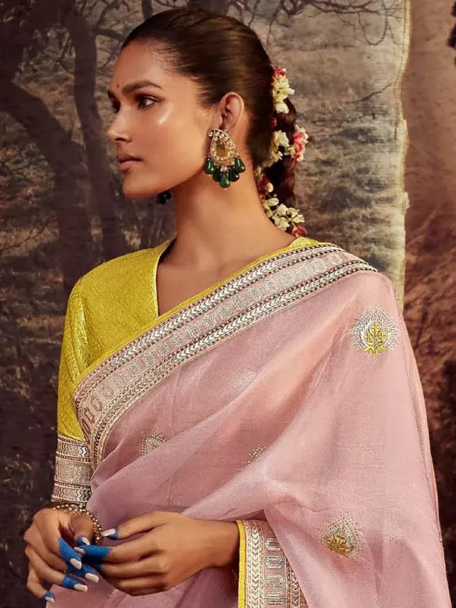 Pink embroidered saree with yellow blouse, floral hair accessory, and green statement earrings