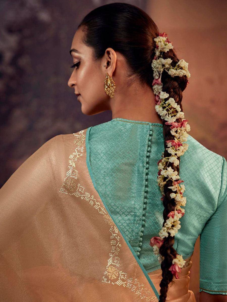 Woman in teal designer saree with floral braid, gold earrings, and embroidered blouse