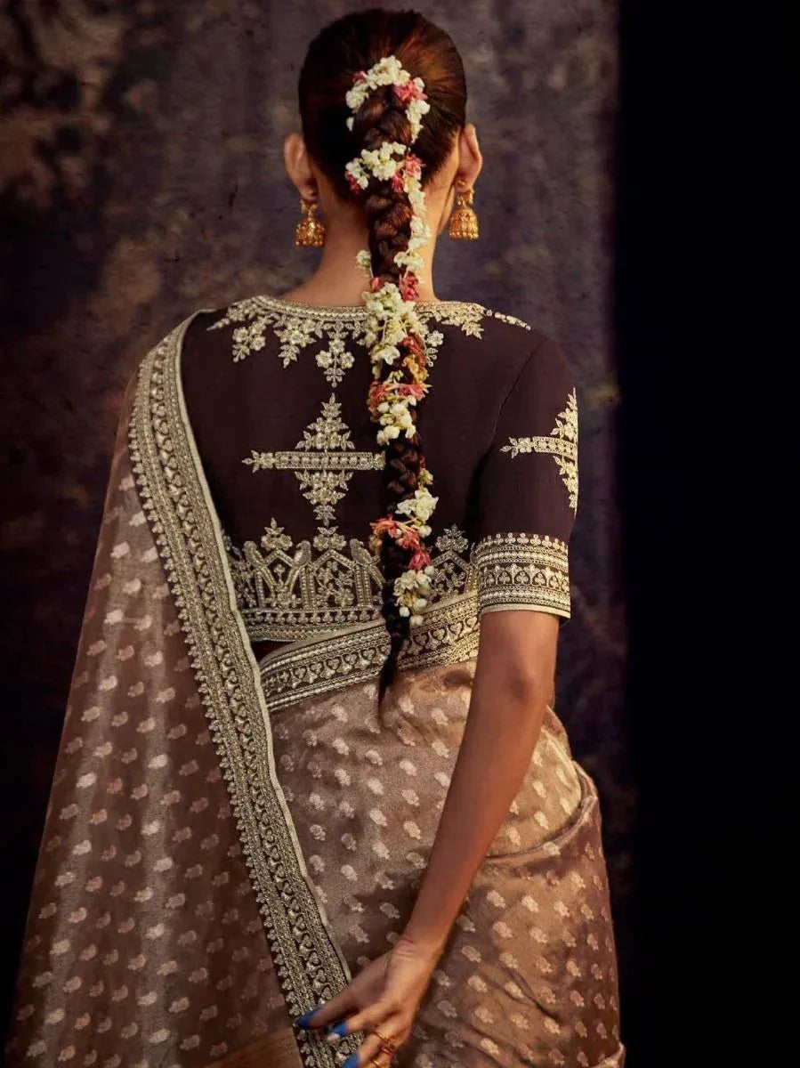 Back view of woman in embroidered Indian saree with floral braid, gold jewelry, and detailed blouse design