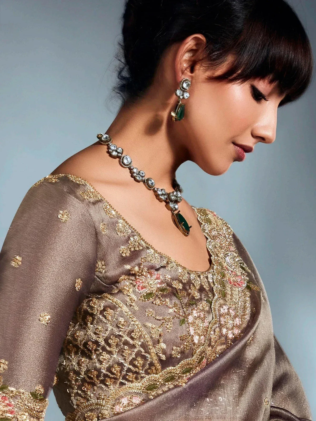 Elegant woman in embroidered ethnic gown with green stone jewelry, perfect for Indian occasions.