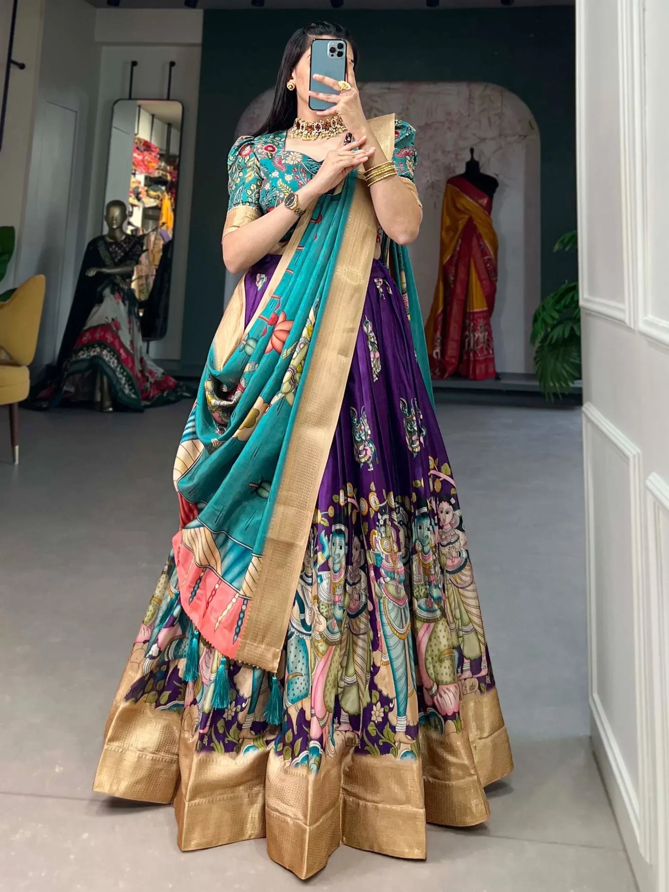 Woman in vibrant purple and teal printed lehenga choli with gold border, taking mirror selfie in boutique
