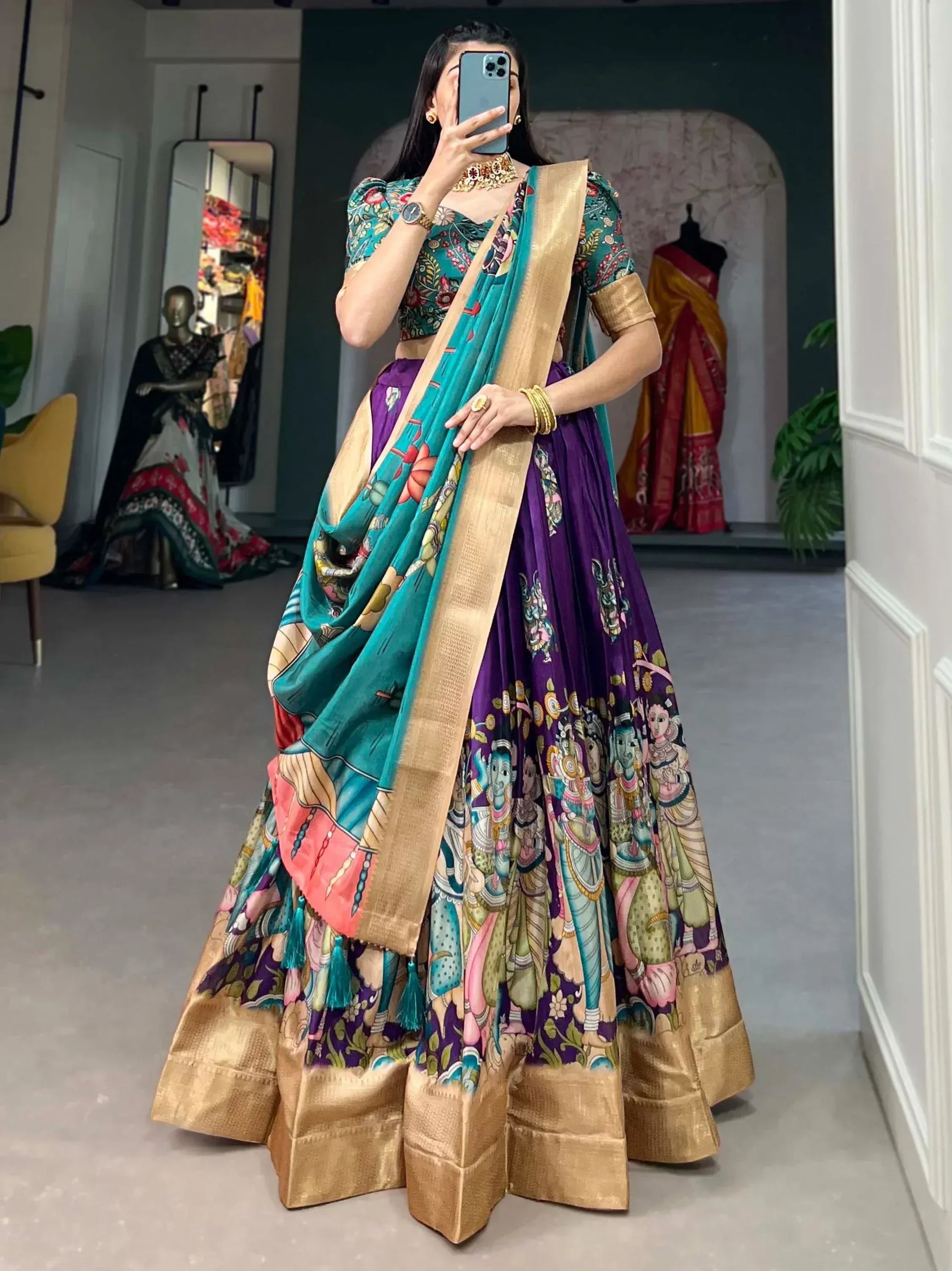 Woman in vibrant purple and teal printed lehenga choli with gold border, taking mirror selfie in boutique
