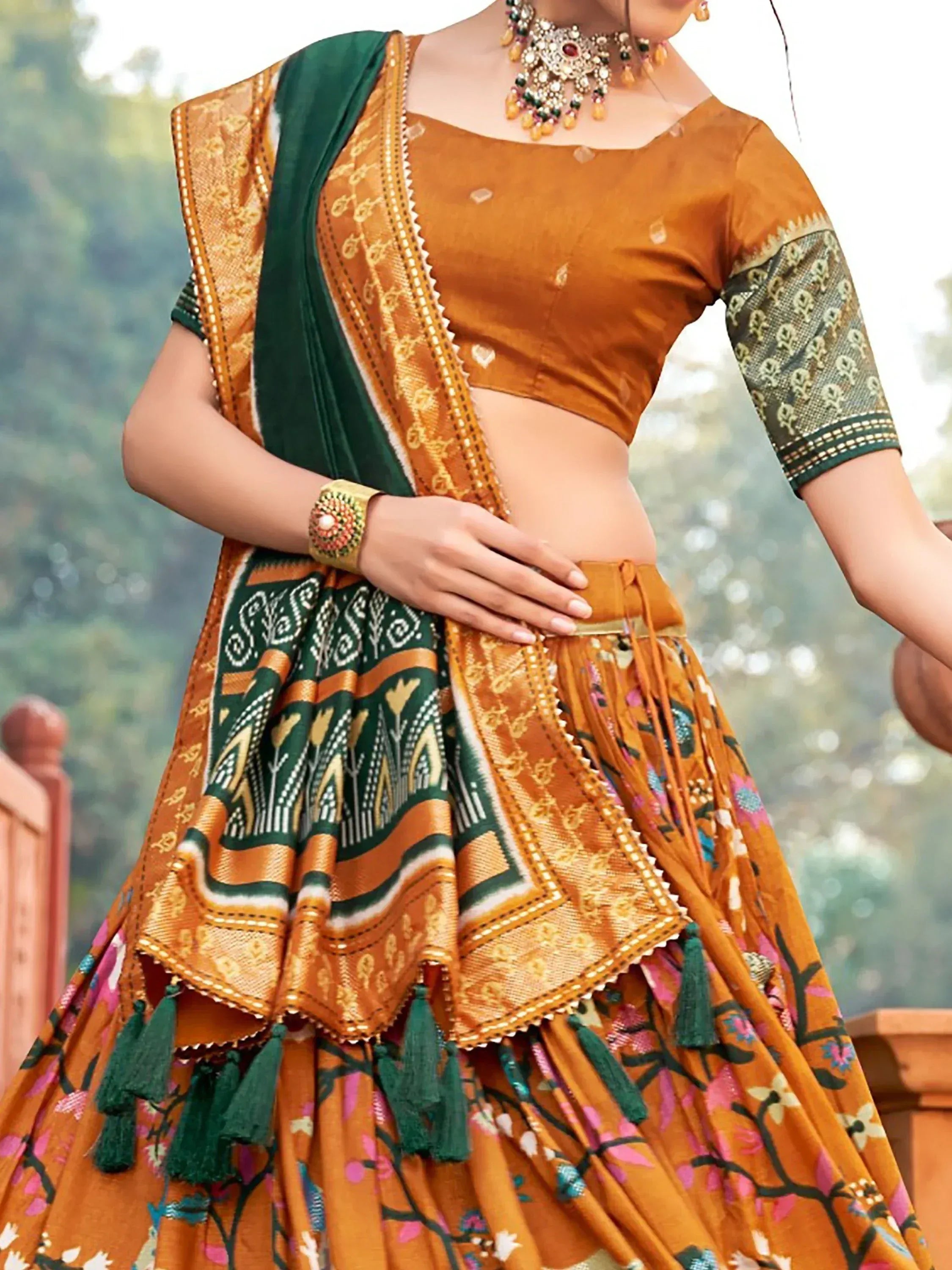 Orange and green designer lehenga choli with floral print, tassels, and traditional jewelry for Indian ethnic wear