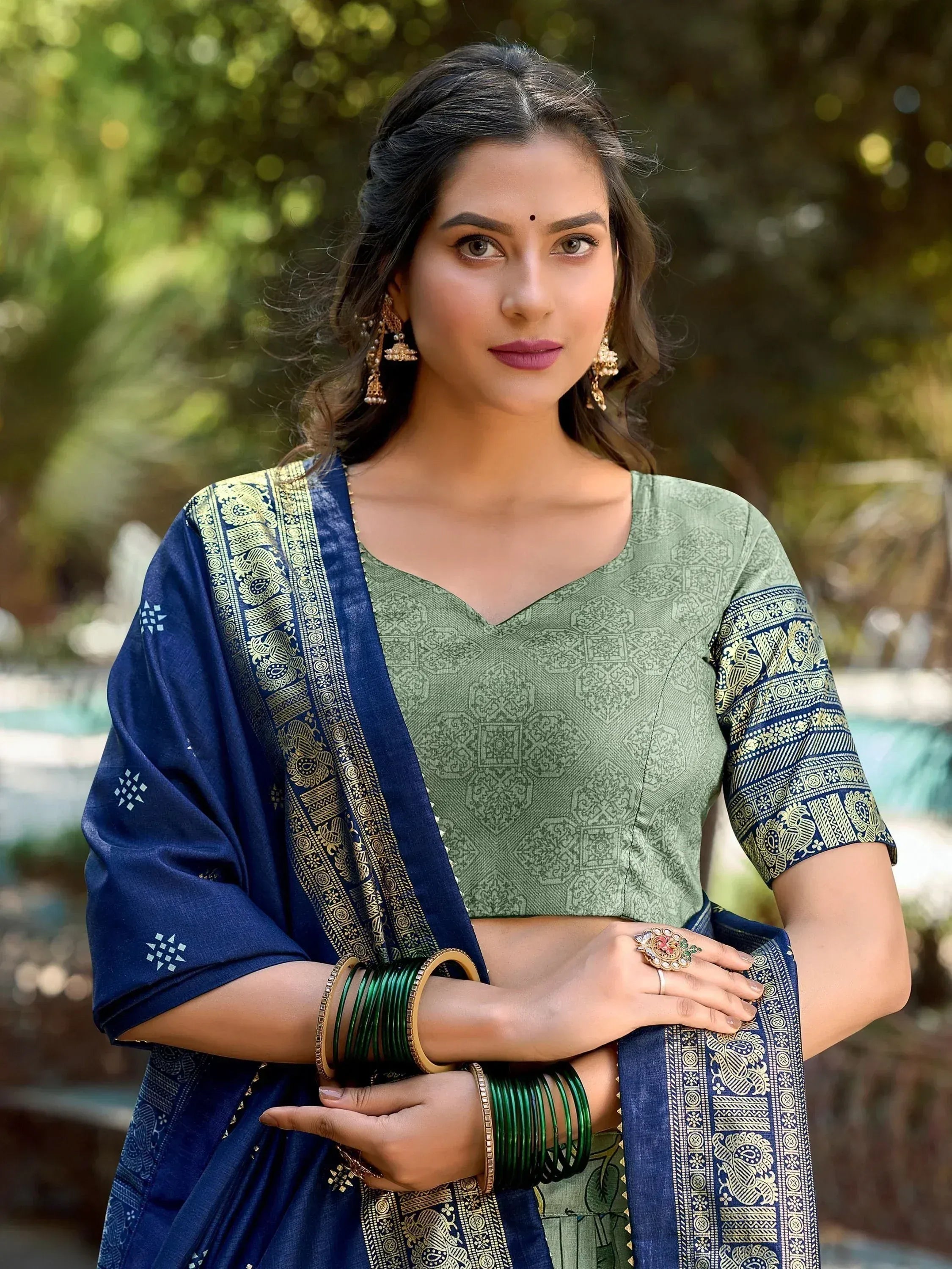 Woman in green printed blouse with blue saree, gold embroidery, and traditional jewelry for ethnic wear