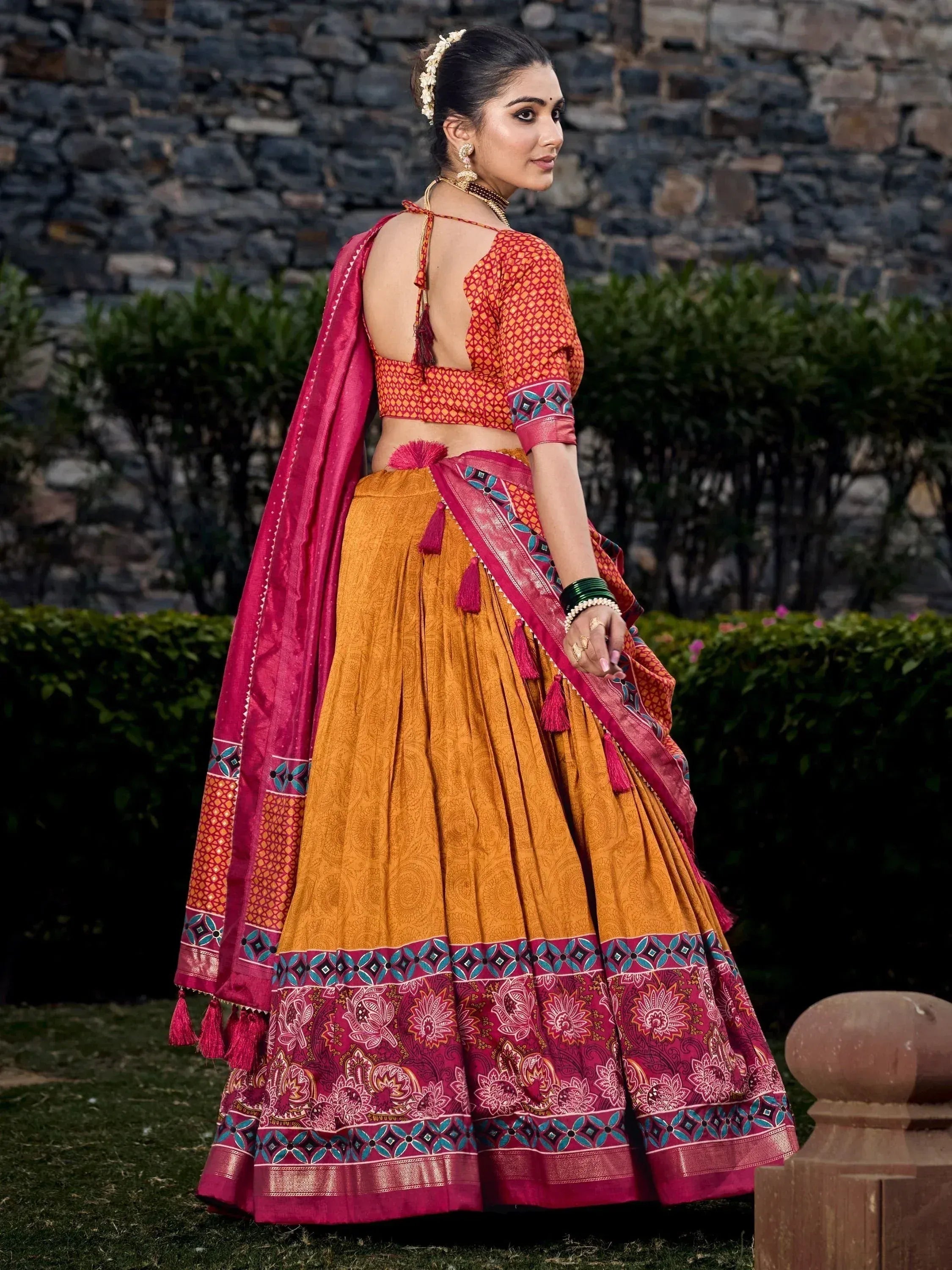 Woman in vibrant orange and pink printed lehenga choli with tassels, perfect for Indian ethnic occasions