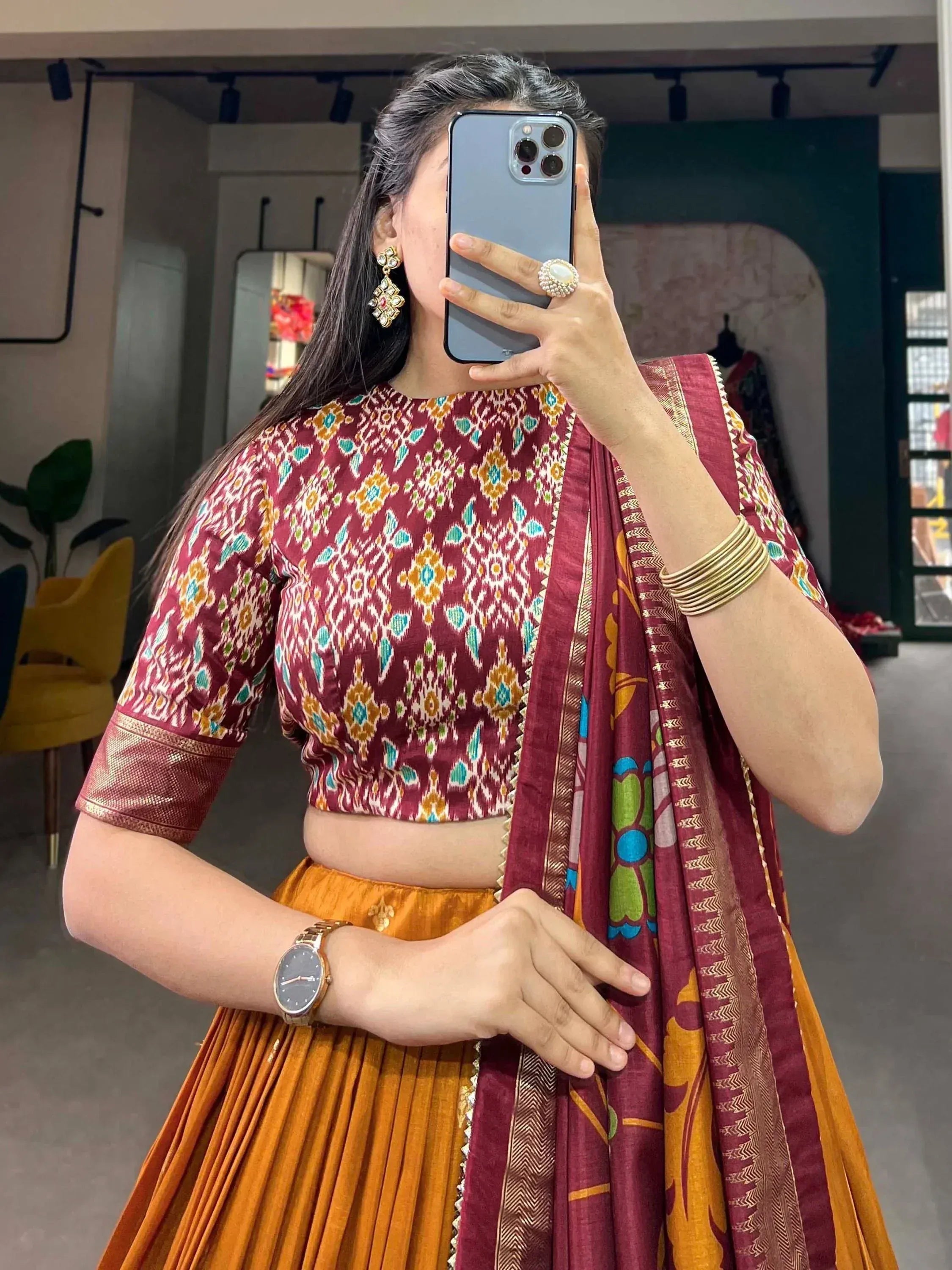 Woman in maroon ikat crop top with orange pleated skirt and matching dupatta, ethnic Indian wear
