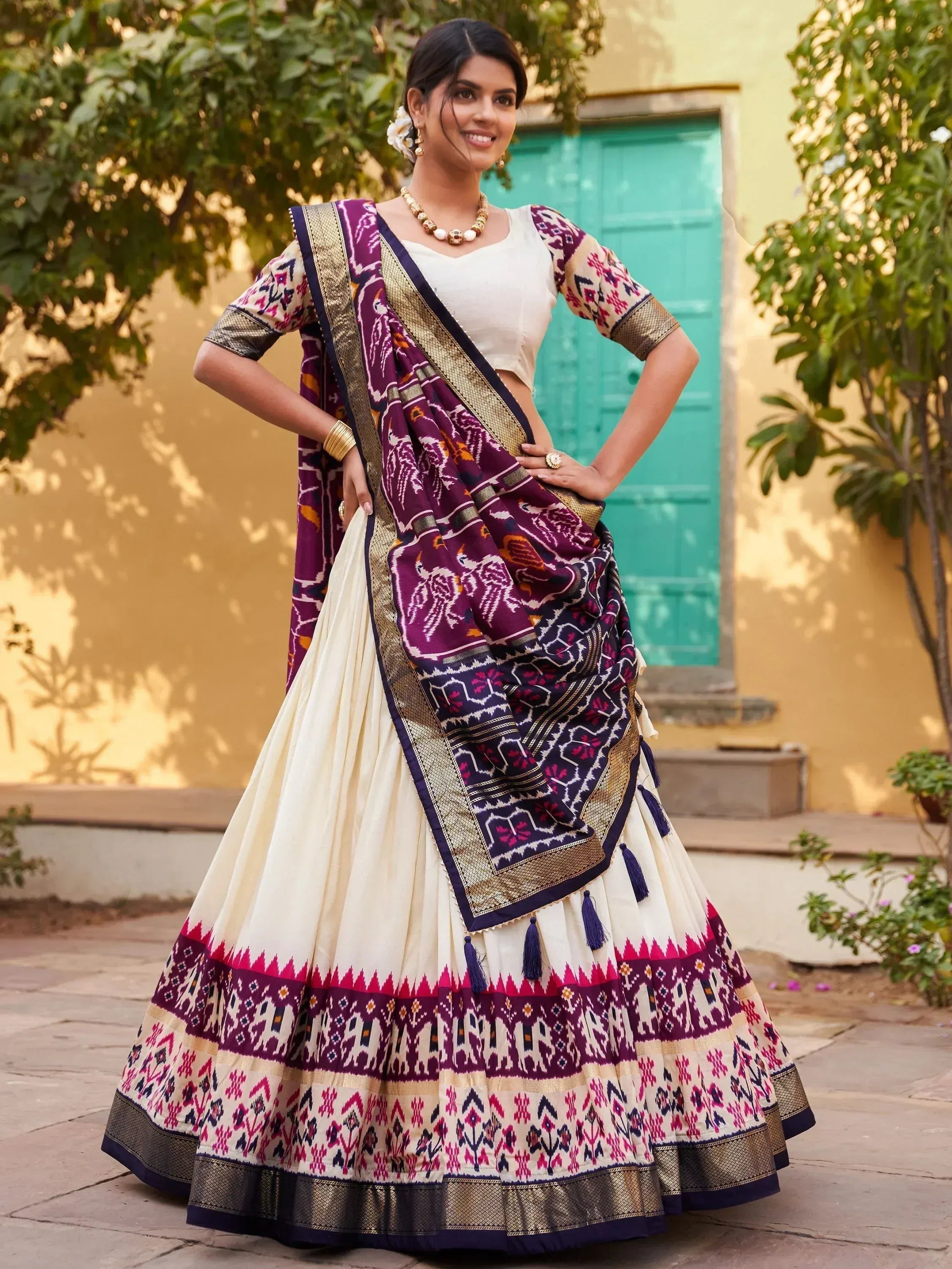 Woman in cream and purple printed lehenga choli with gold border, ethnic Indian wear for festive occasions