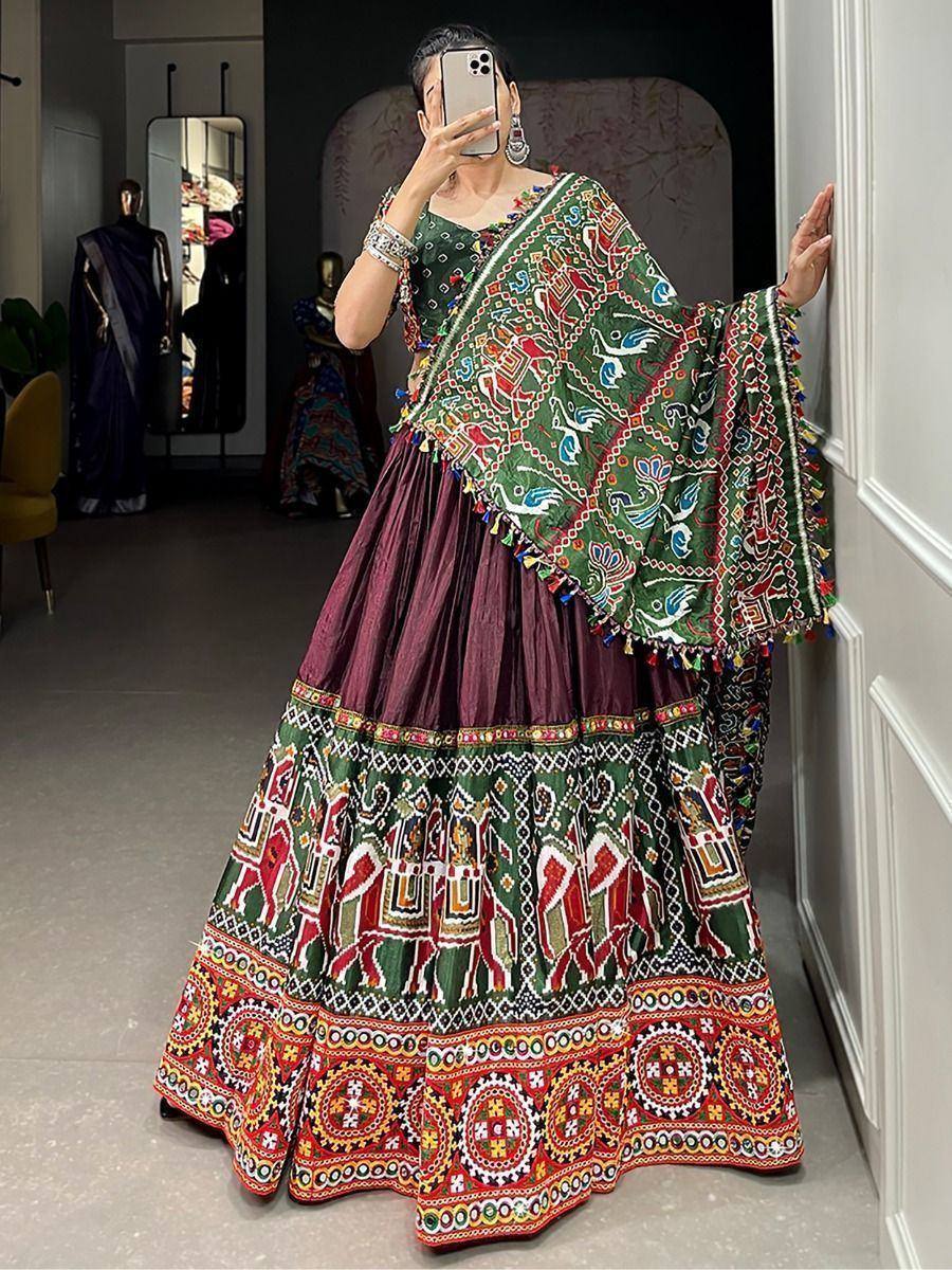 Woman wearing vibrant green and maroon embroidered lehenga choli with mirror work and tassels, perfect for festive occasions.
