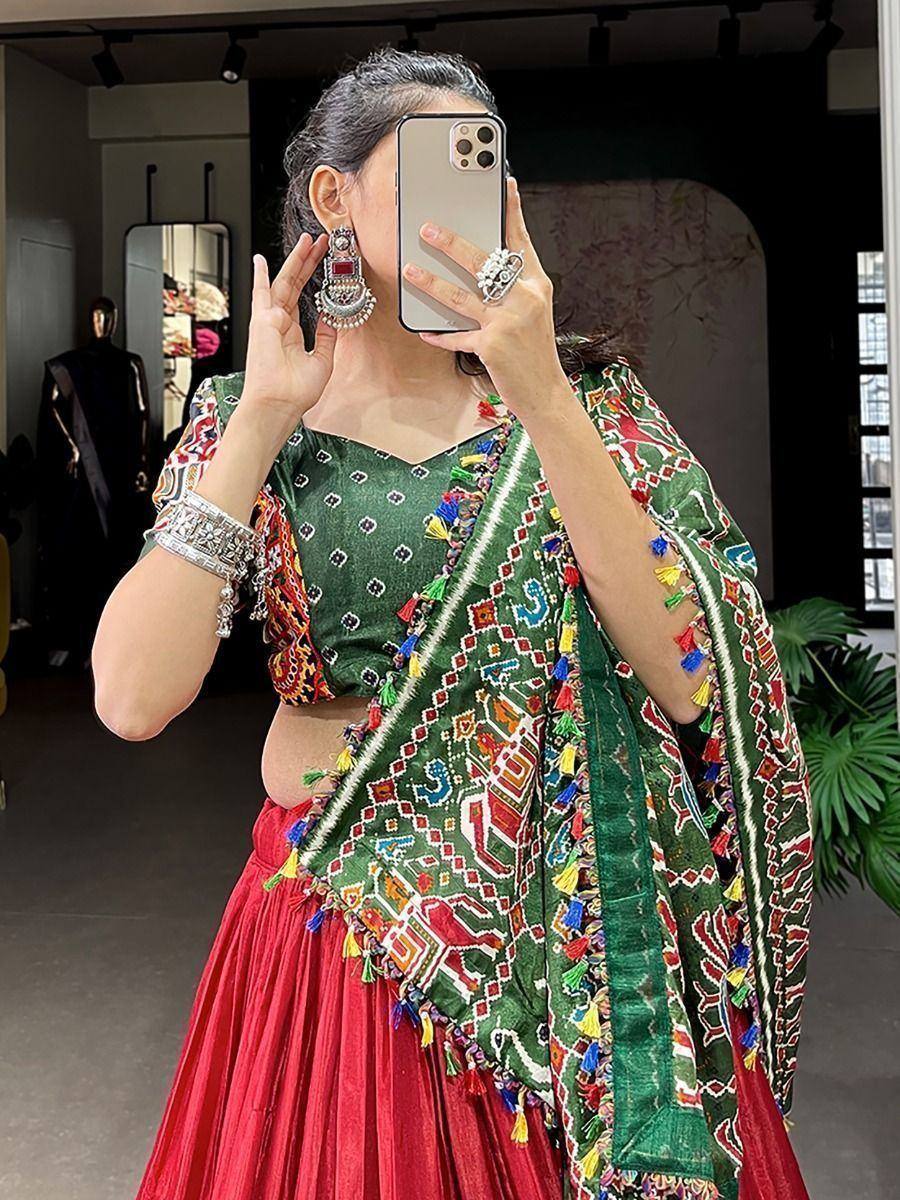 Woman in vibrant green and red ethnic lehenga choli with colorful embroidery and tassels, taking mirror selfie
